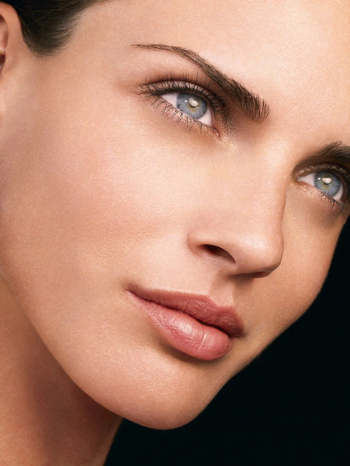 Close-up of a woman’s face, showing smooth skin, blue eyes, and nude lips.