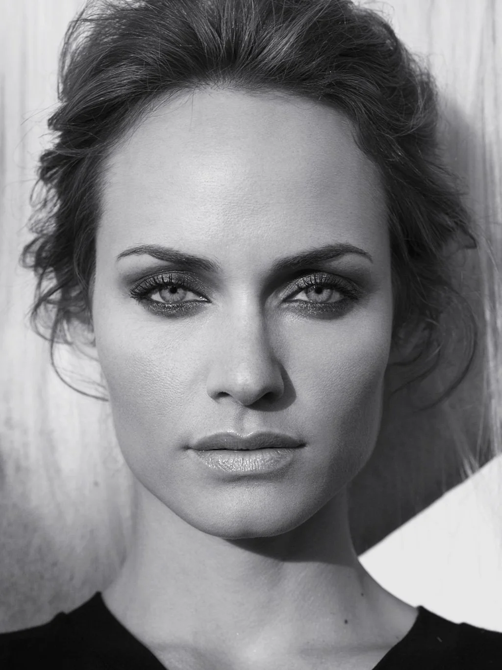 Close-up black and white portrait of a woman with styled hair, makeup, and a serious expression.