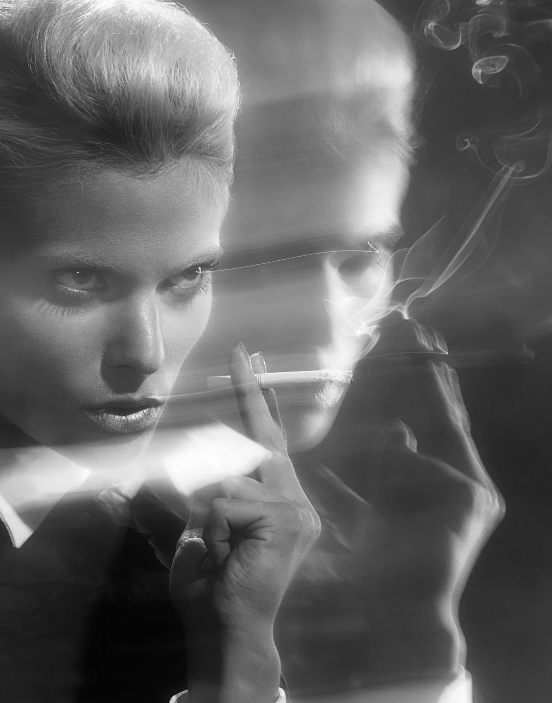 A black-and-white photo of a woman with blonde hair, holding a cigarette, with her face in focus and her reflection or a second person blurred in the background, surrounded by smoke.