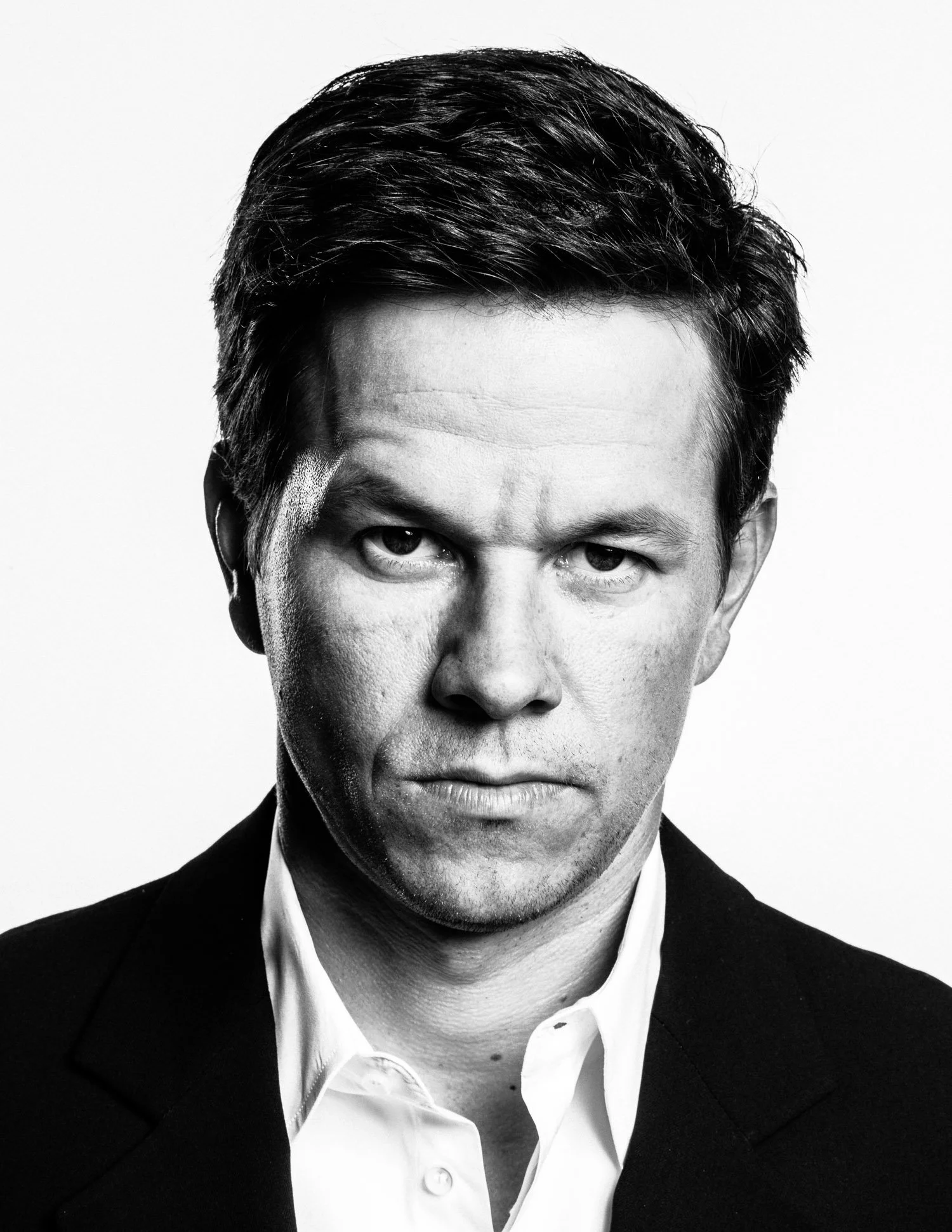 Black and white close-up portrait of MARK WAHLBERG with dark hair, wearing a suit and white shirt, with a serious expression, looking directly at the camera.