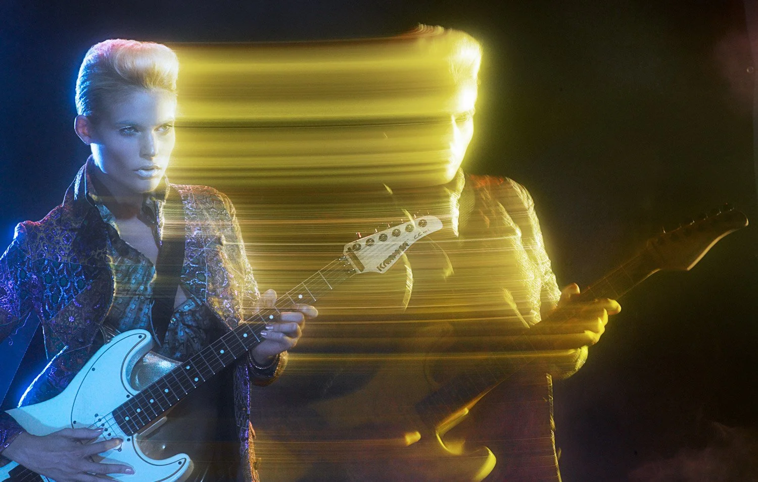A woman playing a white electric guitar and a man playing a guitar, with the scene heavily distorted and streaked by yellow and blue light effects.