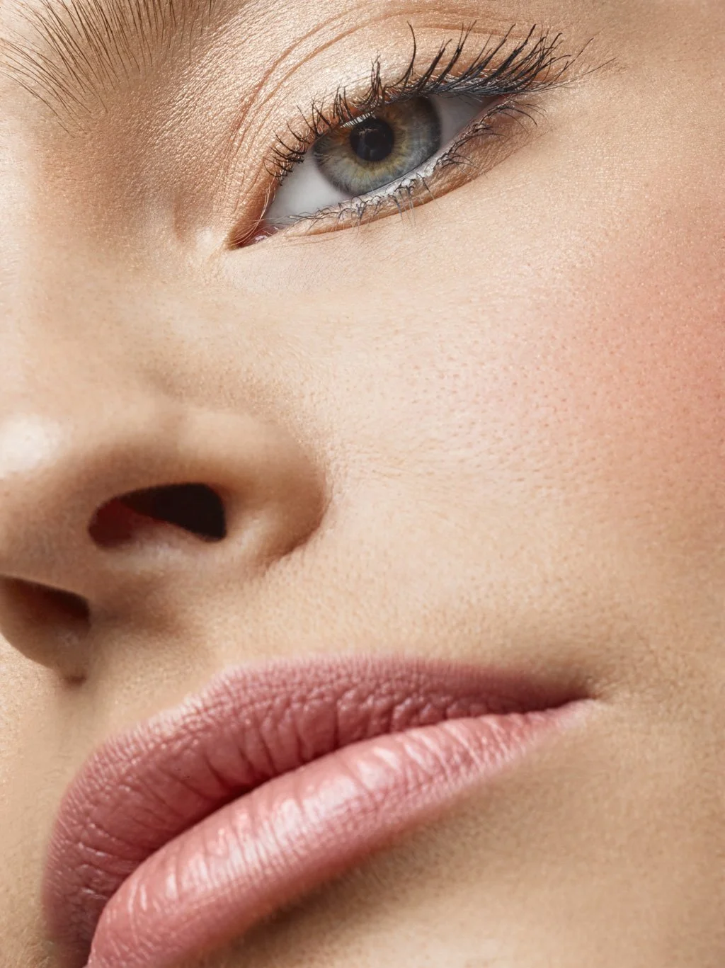 Close-up of a woman's face, showing her eye, nose, and lips with smooth skin and natural makeup.