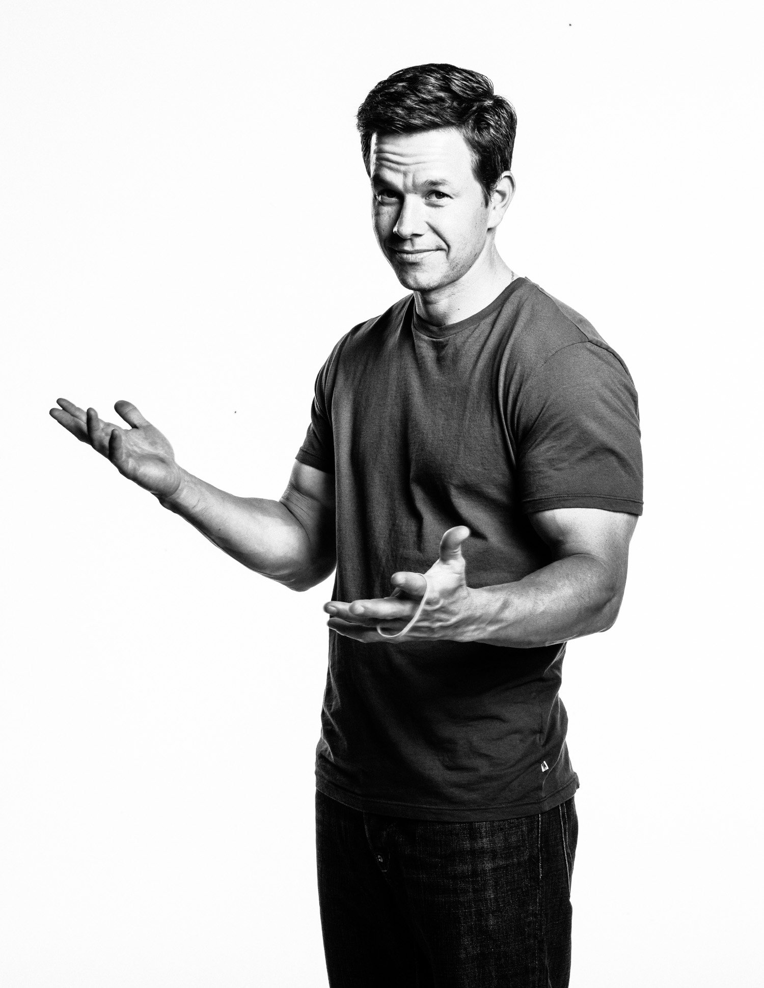 Black and white photo of MARK WAHLBERG in casual clothes gesturing with his hands and looking at the camera against a plain background.