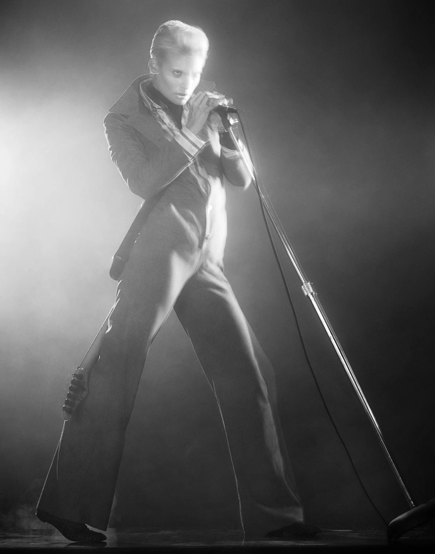 Black and white photo of a woman singing into a vintage microphone on stage, wearing wide-legged pants and a blazer, with a dramatic pose.