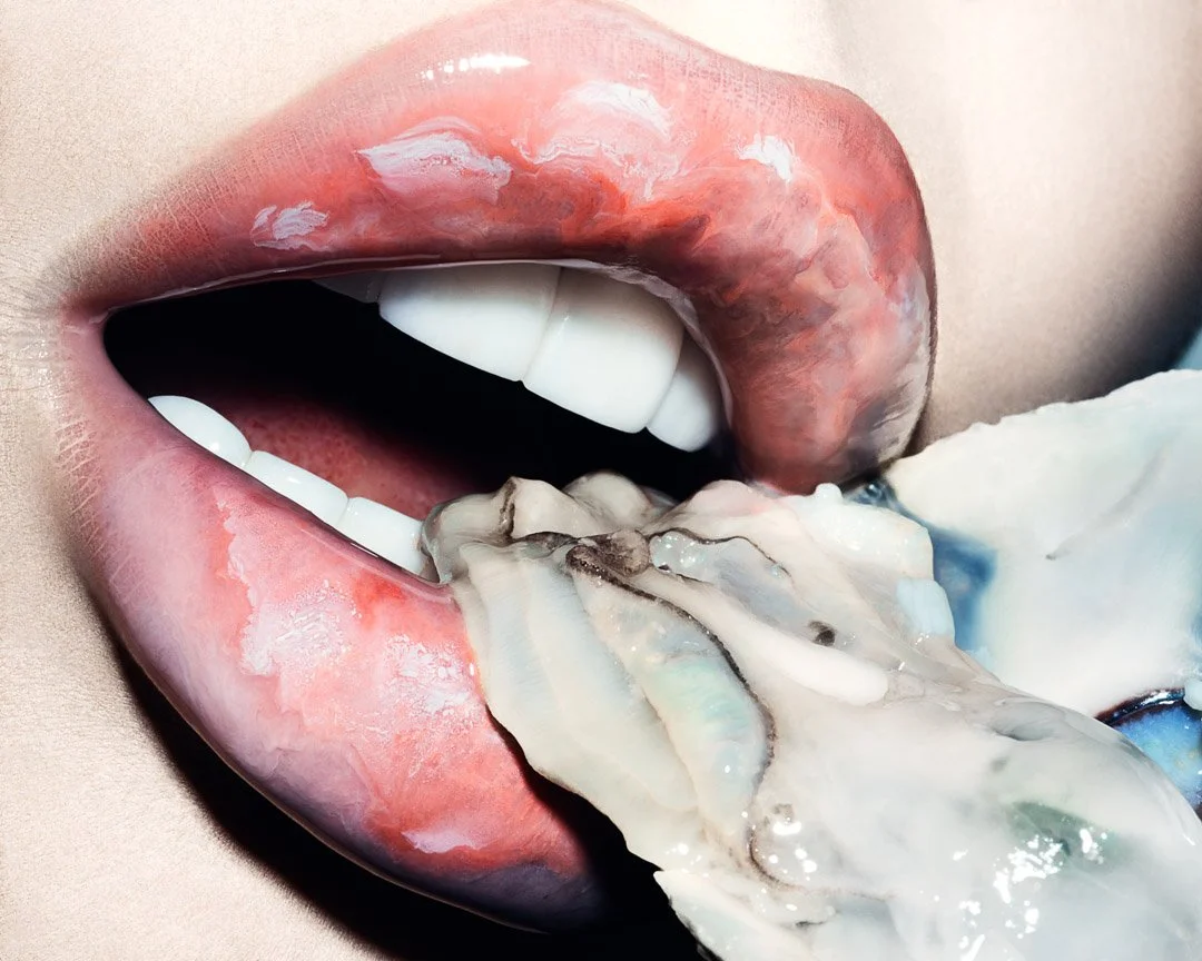 Close-up of a person's mouth with lips slightly parted, licking a large oyster on ice.