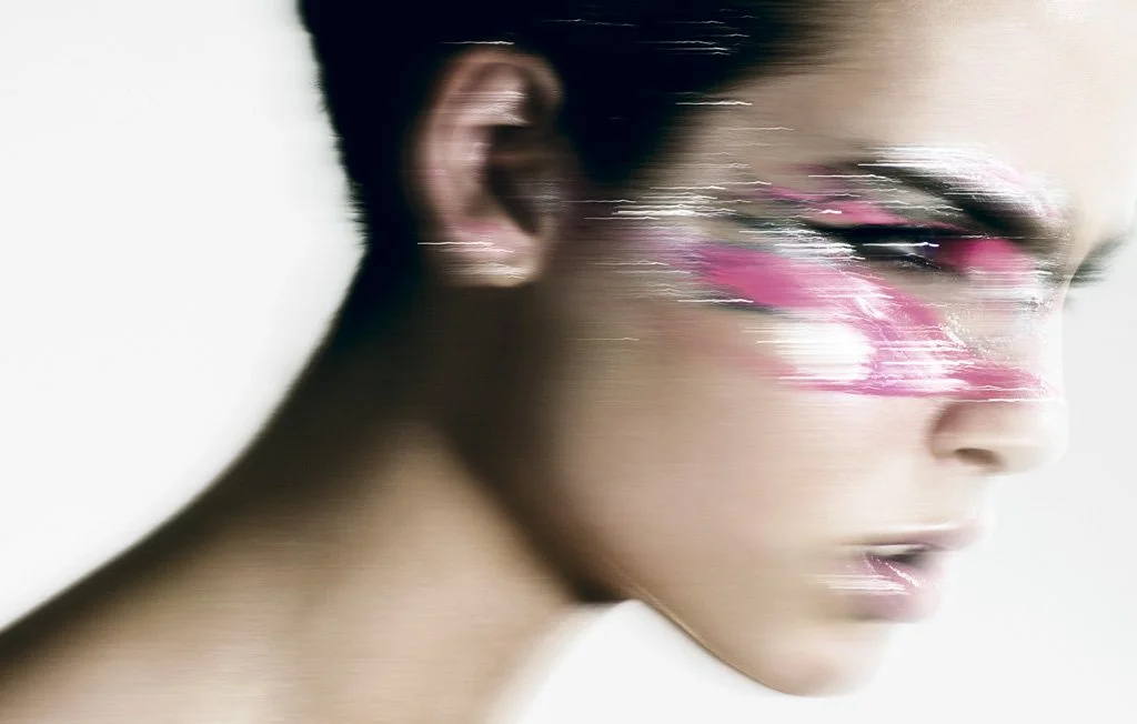 Close-up of a person's face with artistic pink and white makeup near their eye, with a blurred and streaked effect.