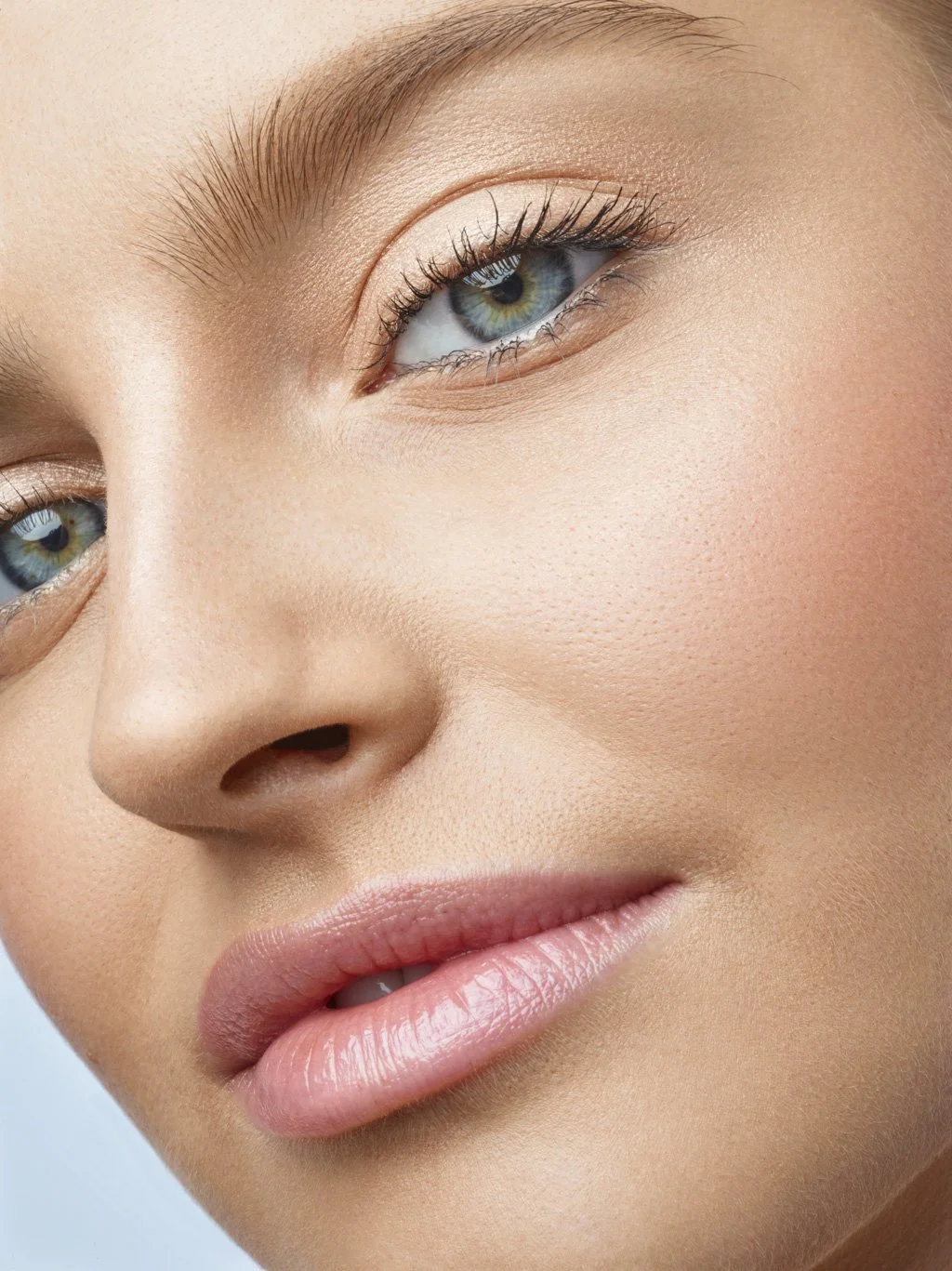 Close-up of a woman's face focusing on her eye, nose, and lips, with clear skin, natural makeup, and light-colored eyes.