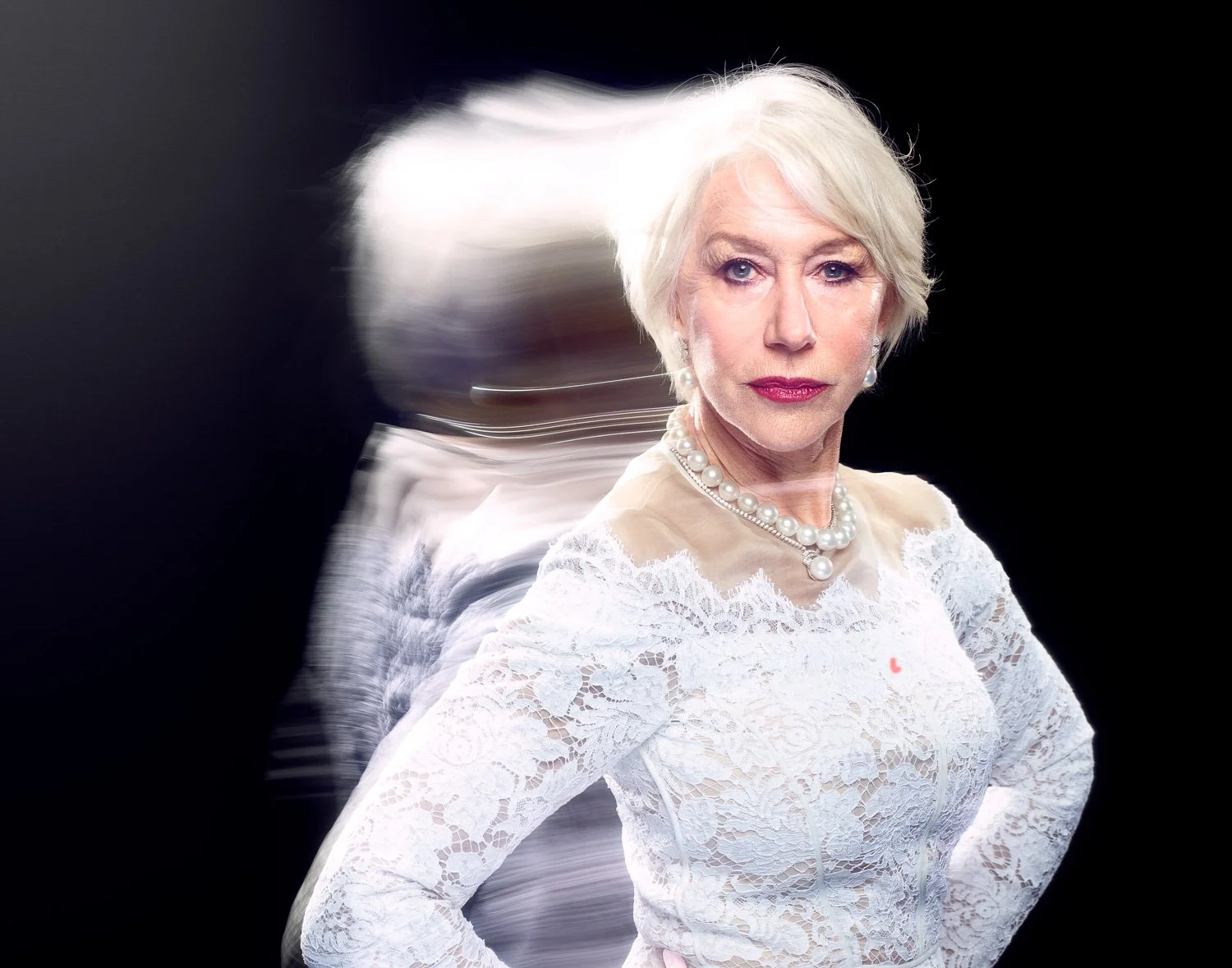 HELEN MIRREN with white hair wearing a white lace dress and pearl necklace, posing against a black background with a motion blur effect.