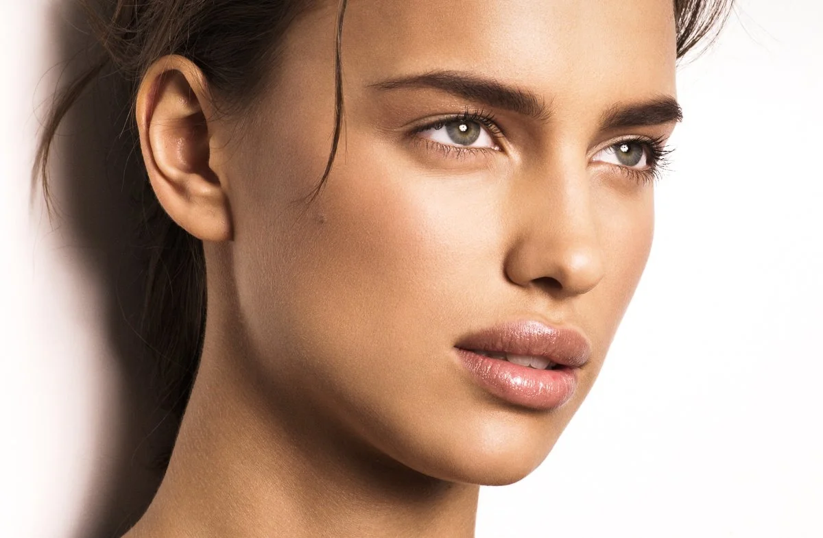 Close-up of a woman with clear skin, light makeup, and brown hair.
