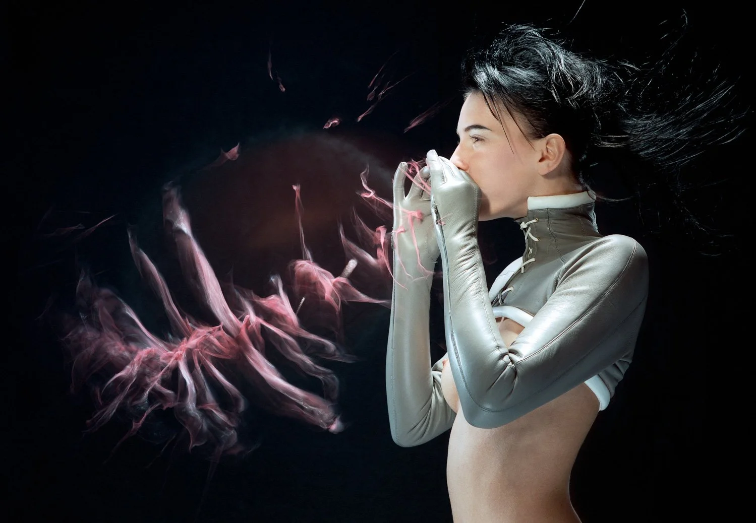 A woman with black hair, wearing a futuristic gray jacket and gloves, blowing pink and white smoke against a dark background.