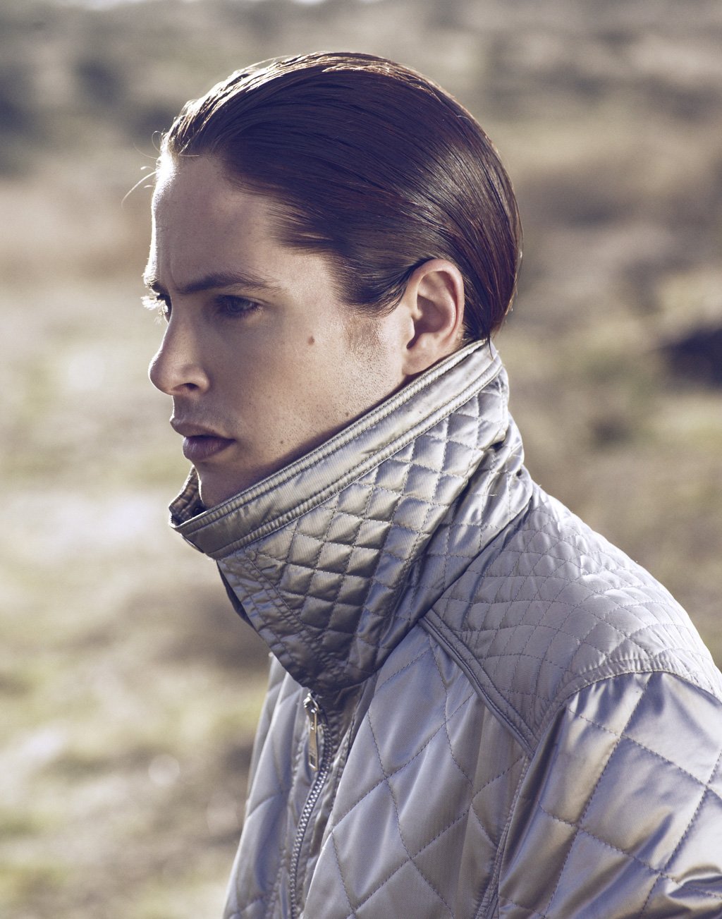A young man with slicked-back hair wearing a quilted metallic jacket outdoors.