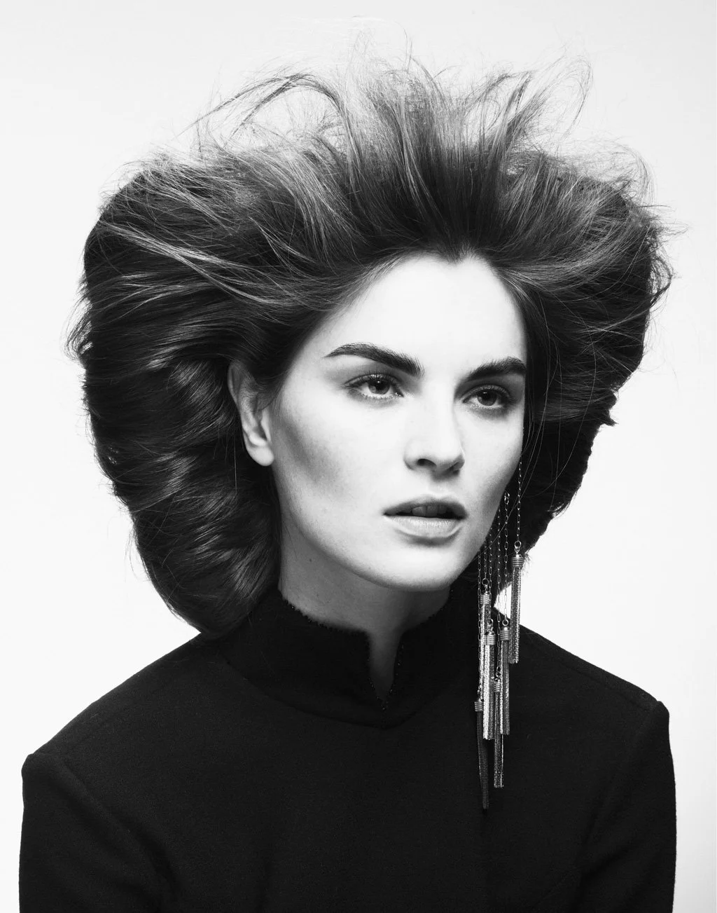 Black and white portrait of a woman with voluminous hair and earrings, wearing a high-neck top.