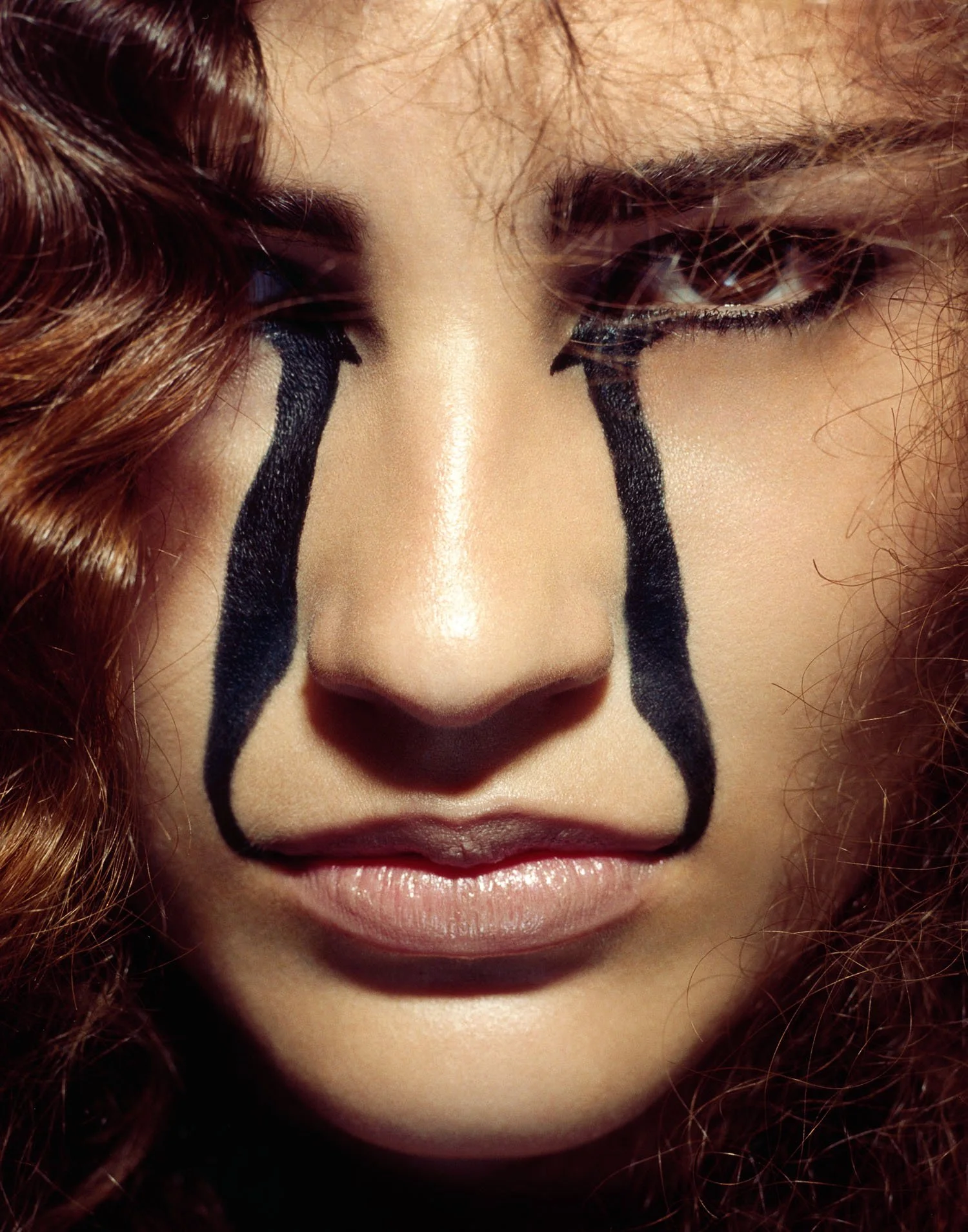 Close-up of a woman's face with black paint that looks like tears streaming down from her eyes.