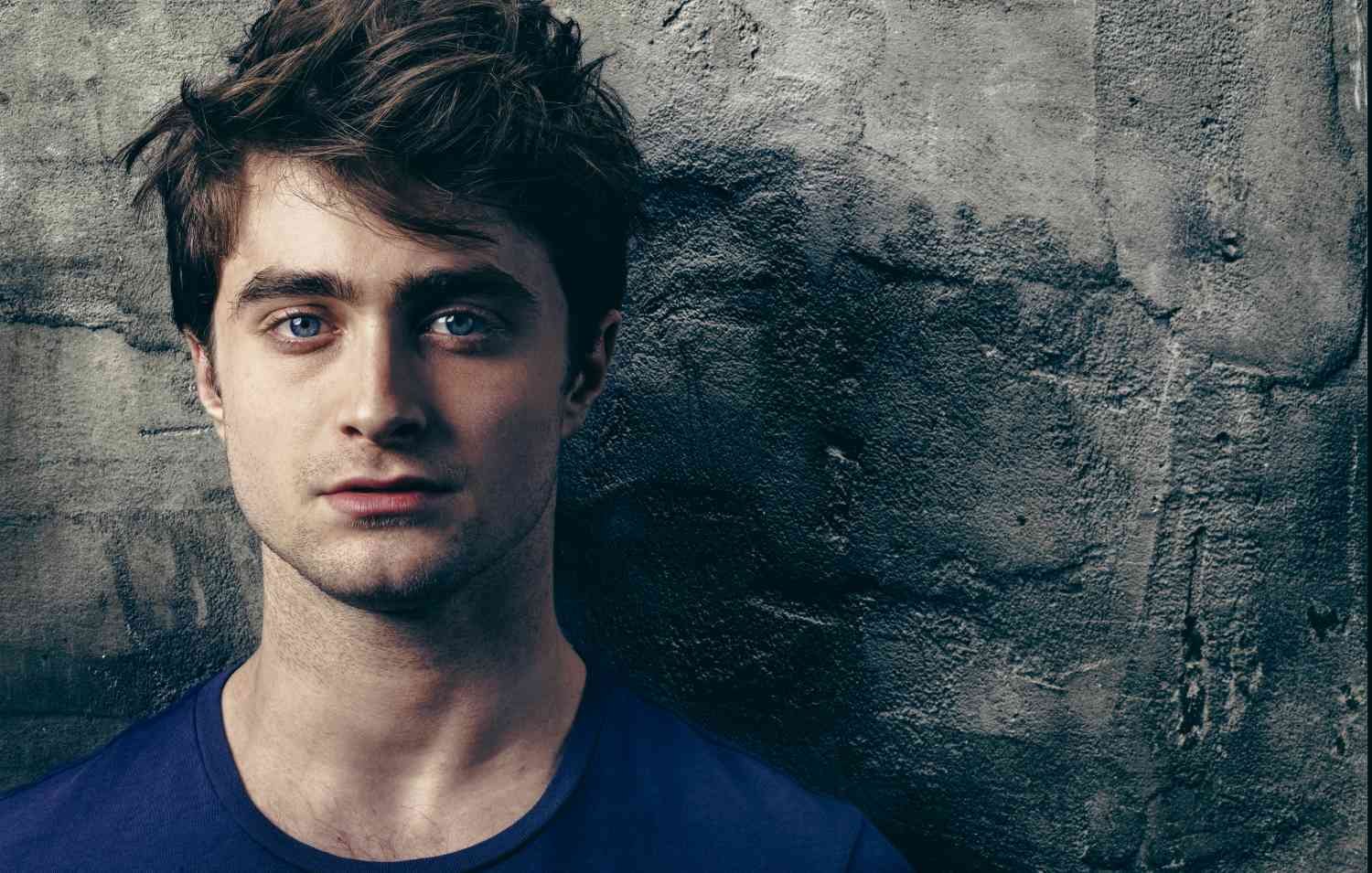 DANIEL RADCLIFFE with blue eyes and brown hair against a textured concrete wall.