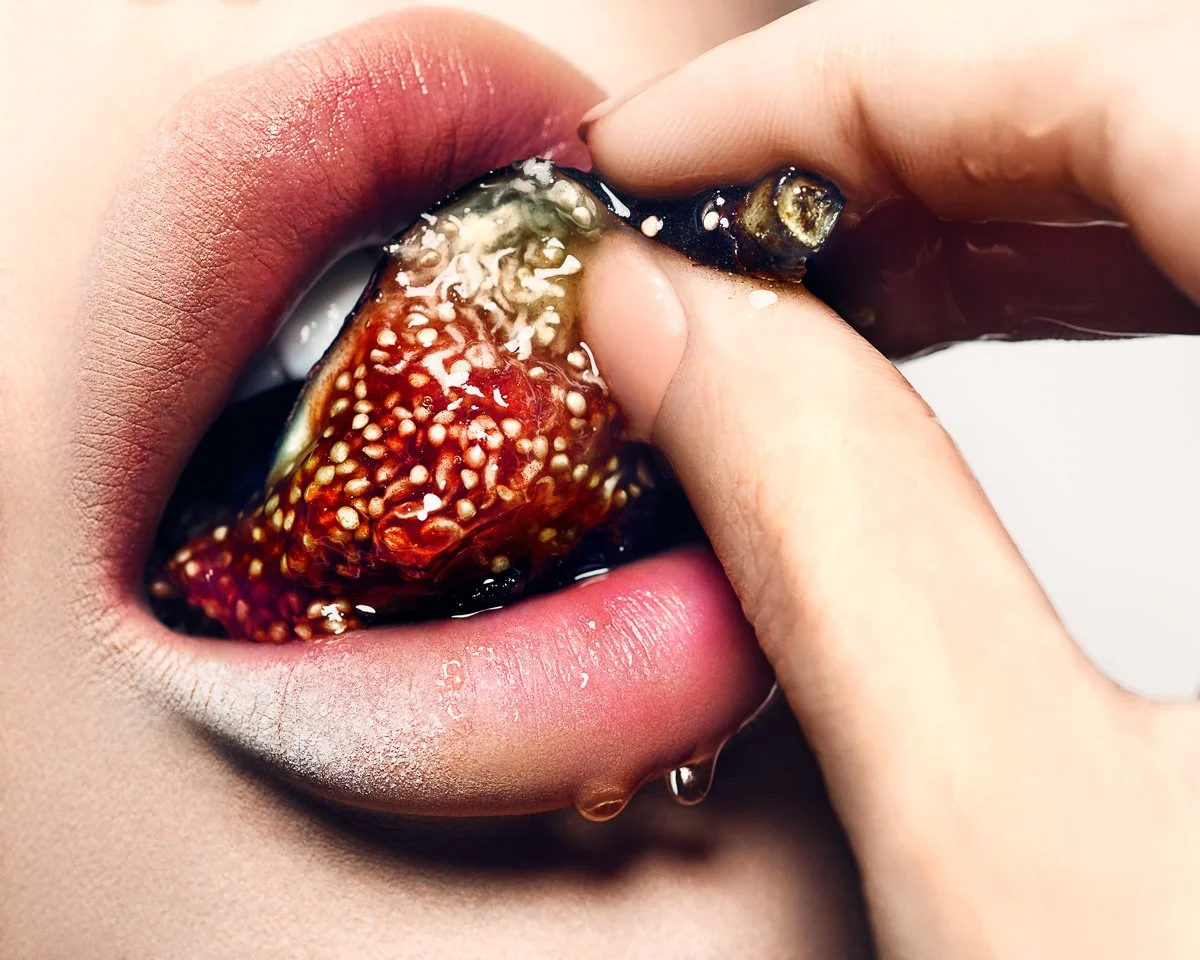 Close-up of lips and tongue with a fig being pressed into them, juice and seeds spilling out.