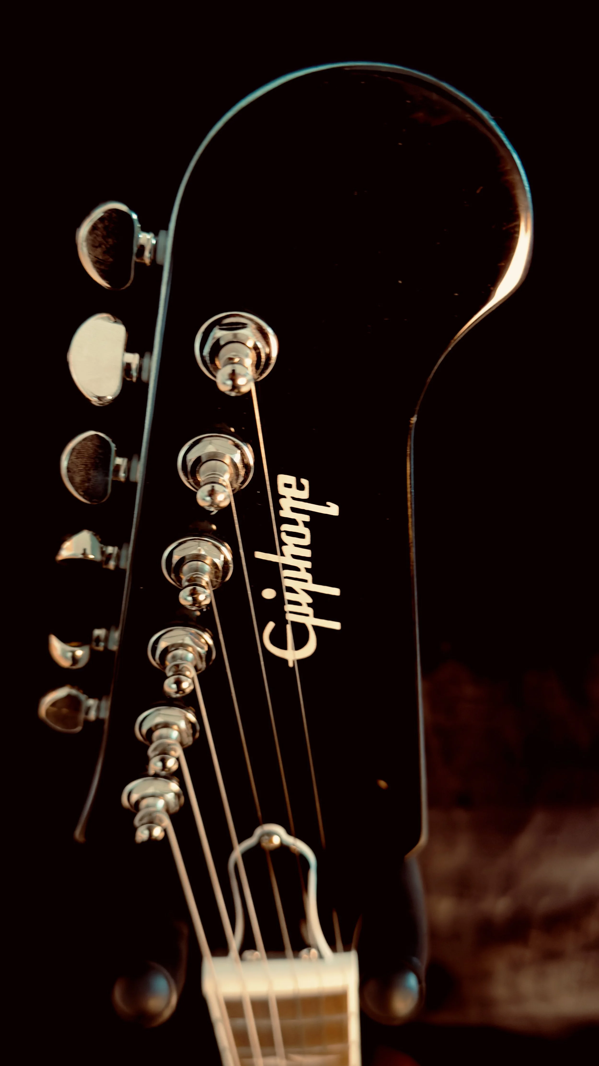 Close-up of a black Epiphone electric guitar headstock with tuning pegs and strings visible.