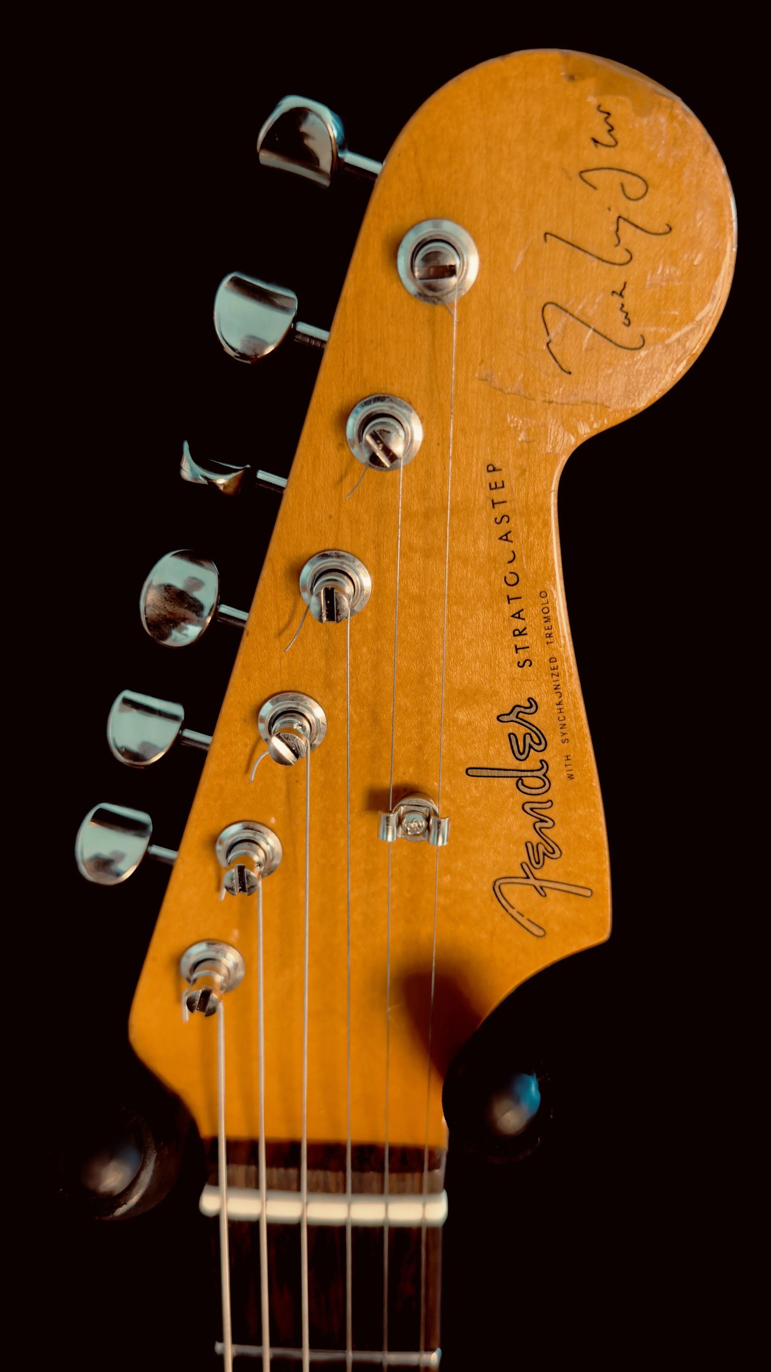 Close-up of a Fender Stratocaster electric guitar headstock with tuning pegs, strings, and handwritten signatures.