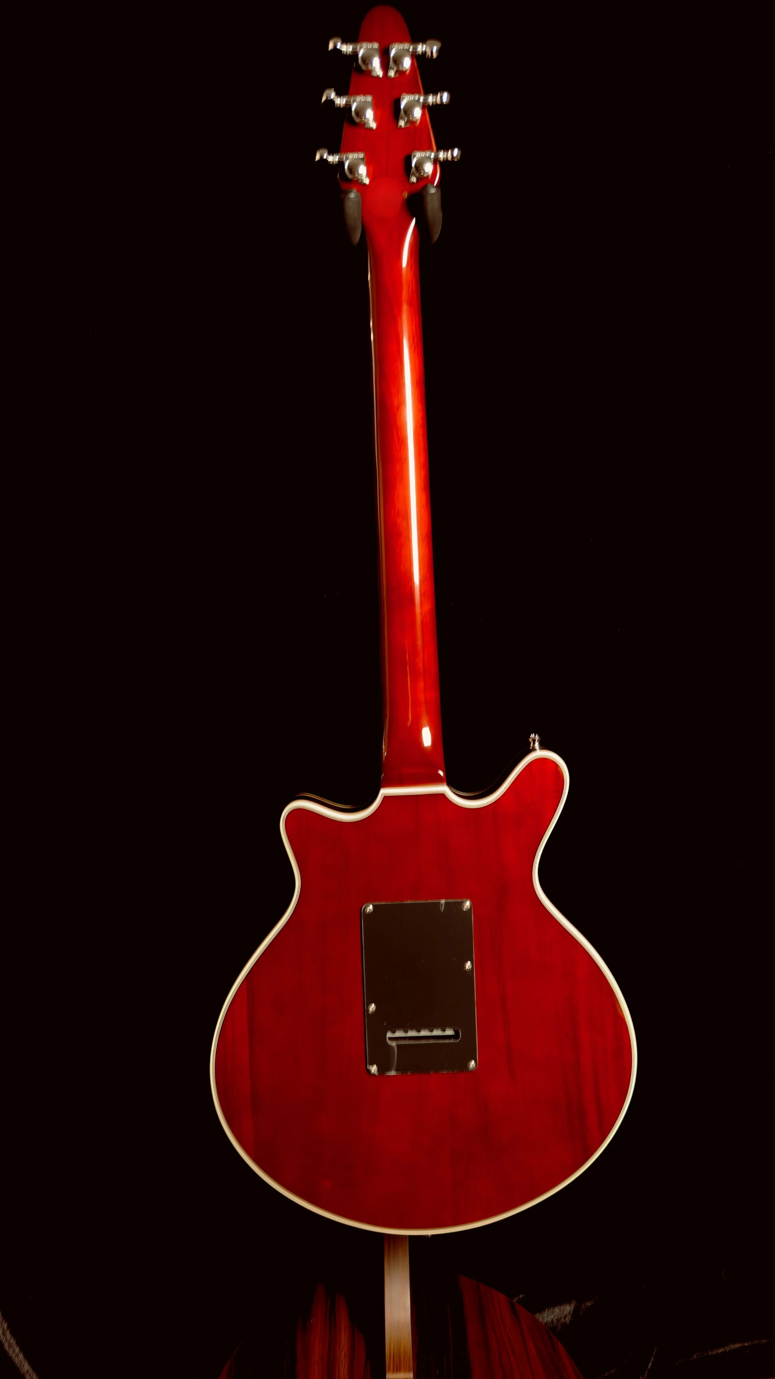 Rear view of a red electric guitar standing upright against a black background.
