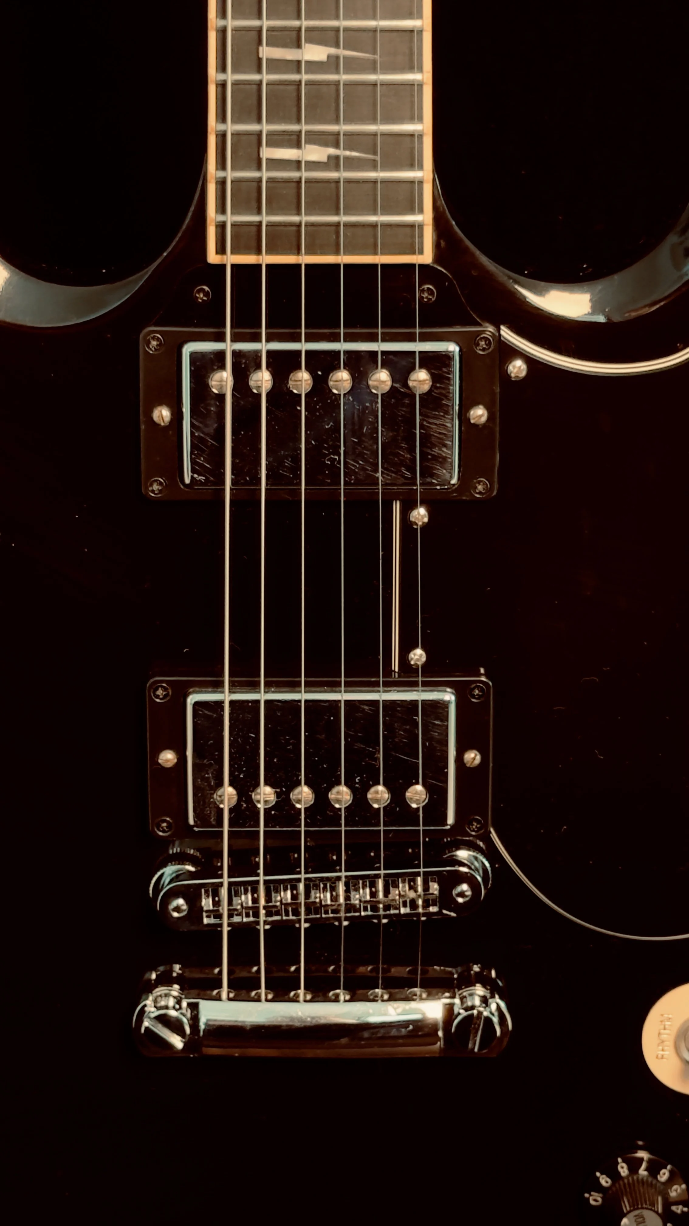 Close-up of a black electric guitar with two humbucker pickups, six strings, and chrome hardware.
