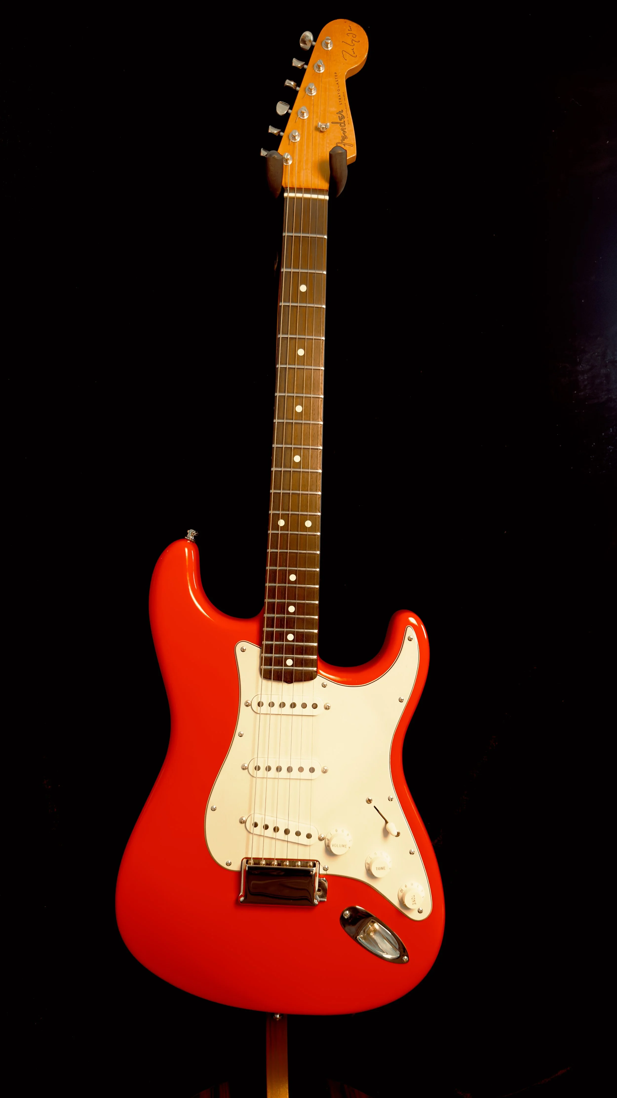 A red electric guitar with a white pickguard and a brown neck and headstock, mounted on a black background.