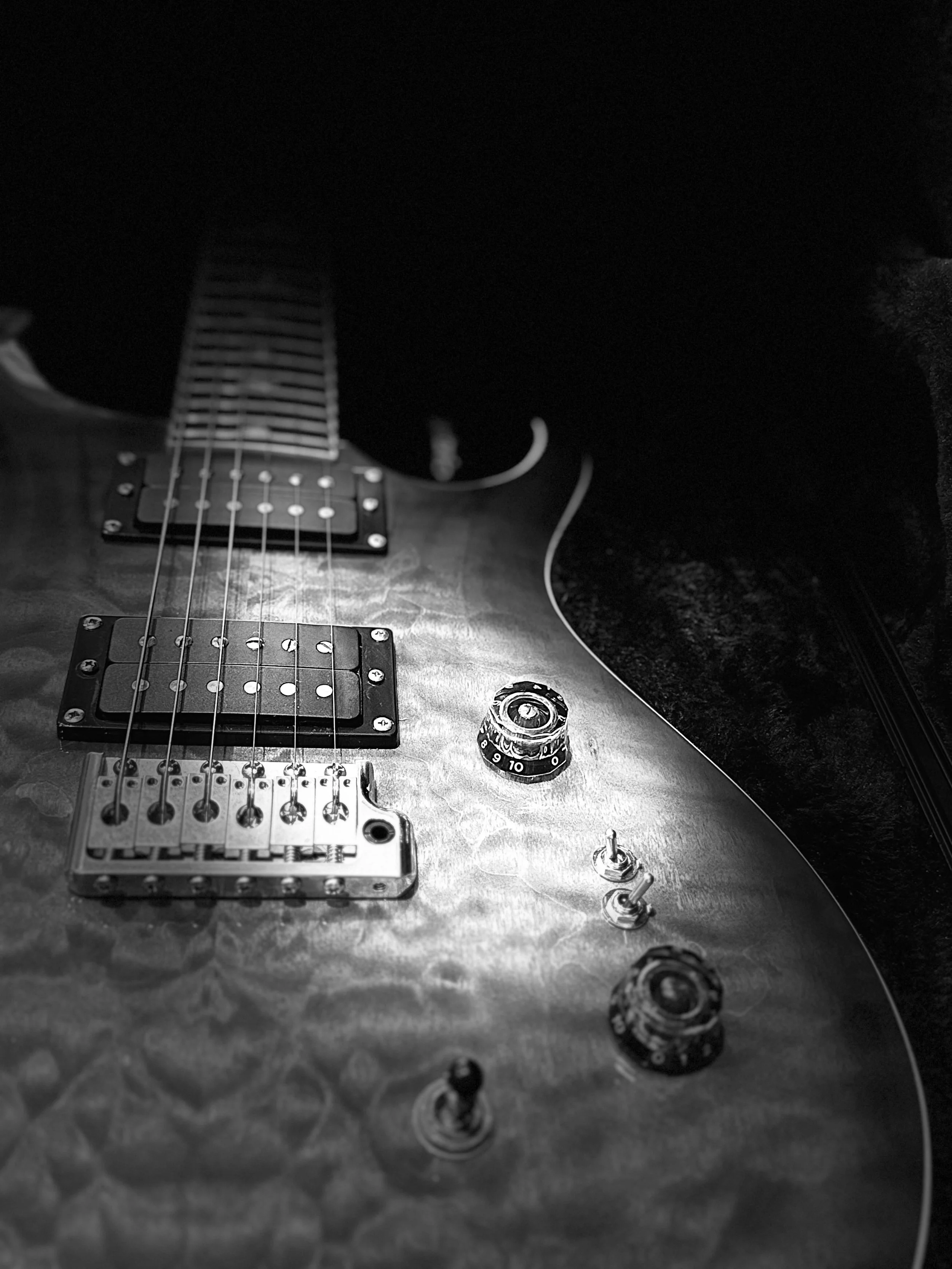 Guitarra elétrica com corpo de madeira, capturada em preto e branco, focada nos controles e nas cordas.