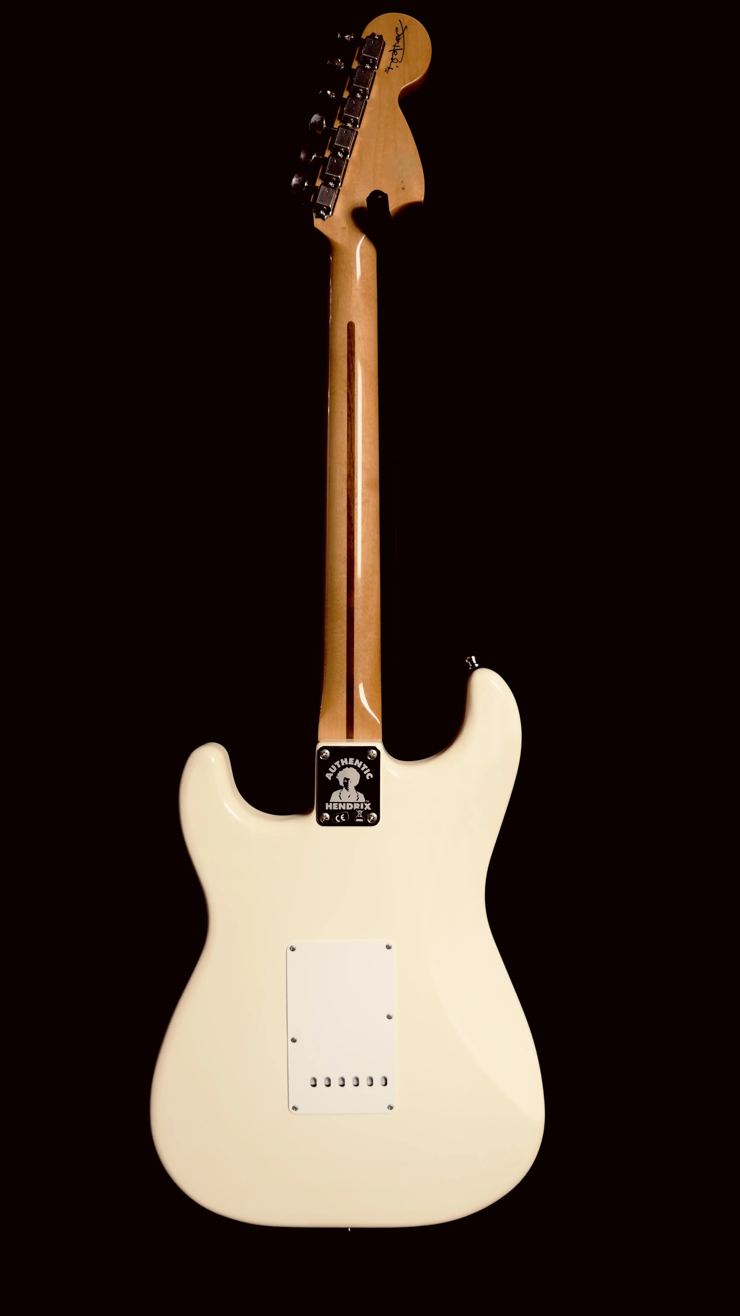 Back of a white electric guitar with maple neck and headstock, signed by Jimi Hendrix, against a black background.