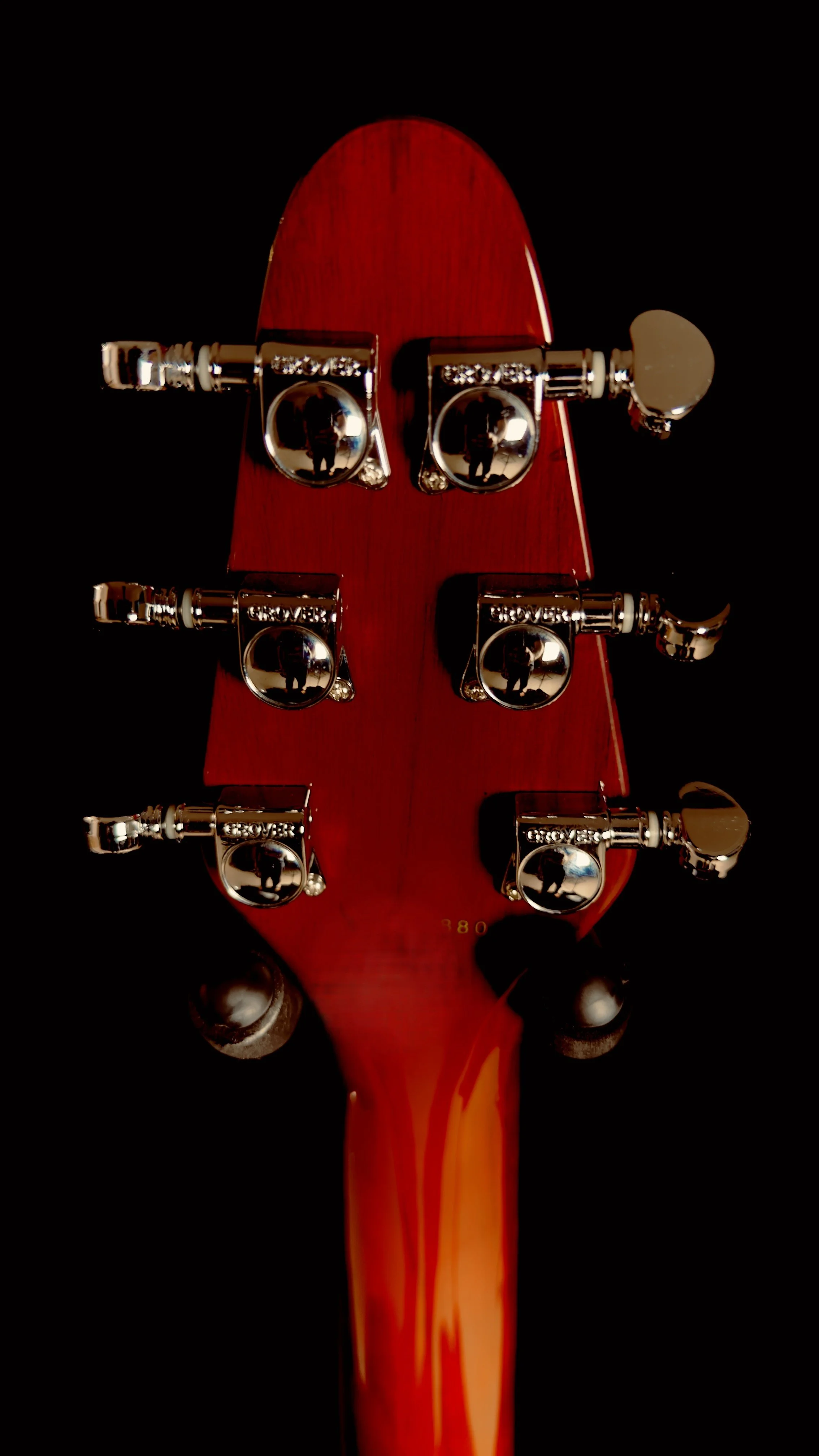Rear view of a red electric guitar's headstock with six chrome tuning pegs against a black background.