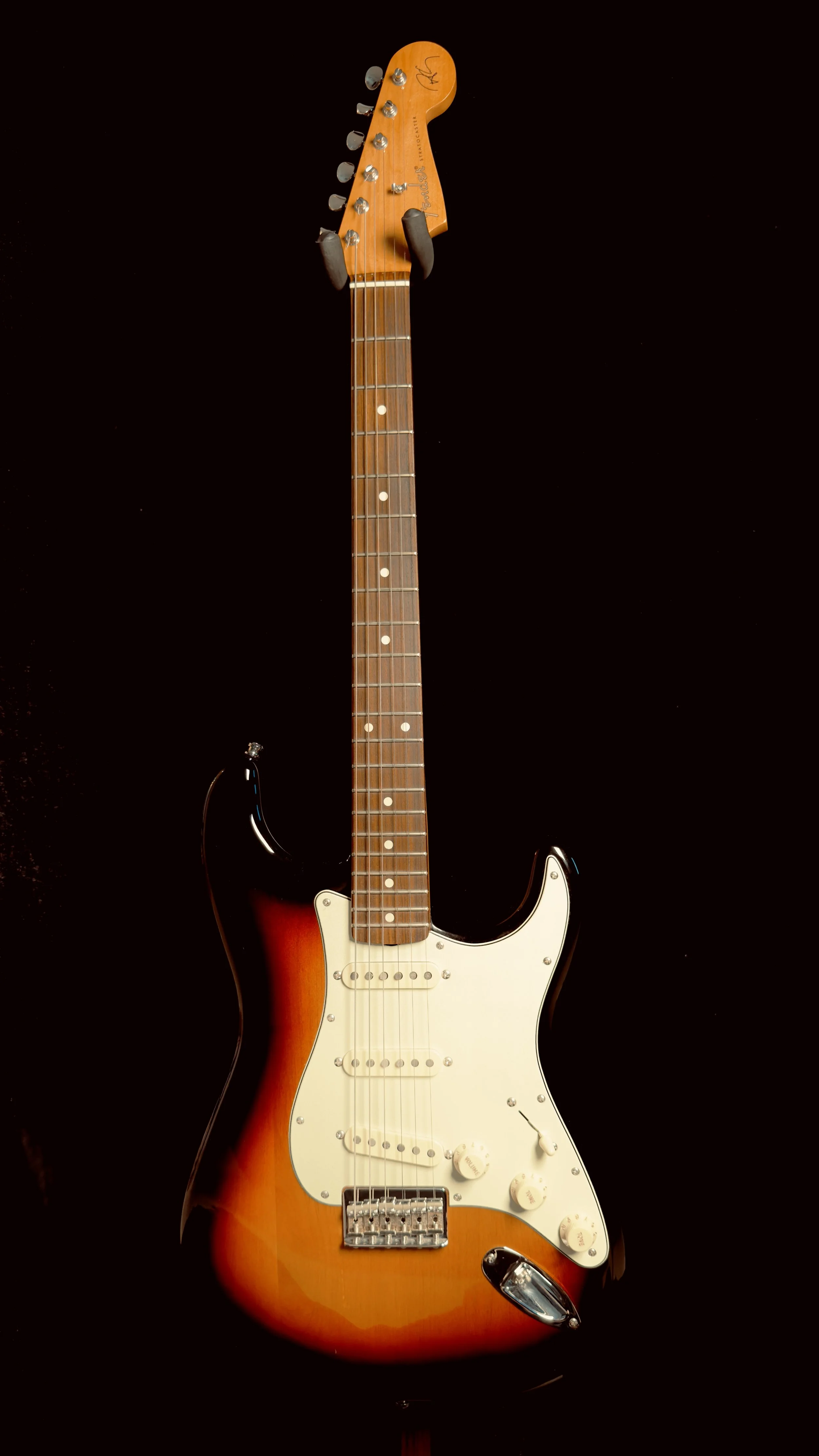 A Fender Stratocaster electric guitar with a sunburst finish, white pickguard, and three pickups, mounted on a black background.