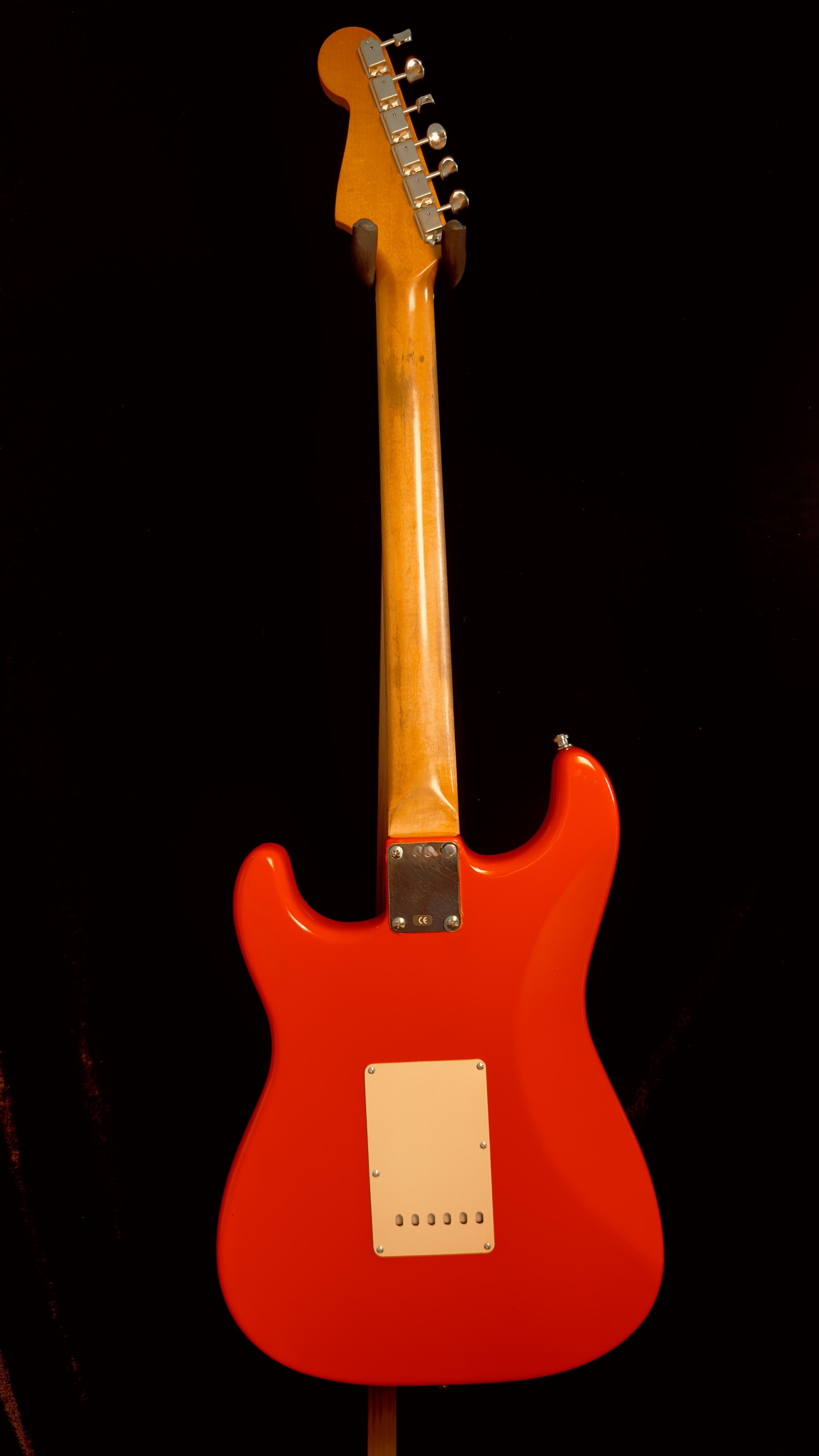 Back of an electric guitar with a red body, wooden neck, and black background.