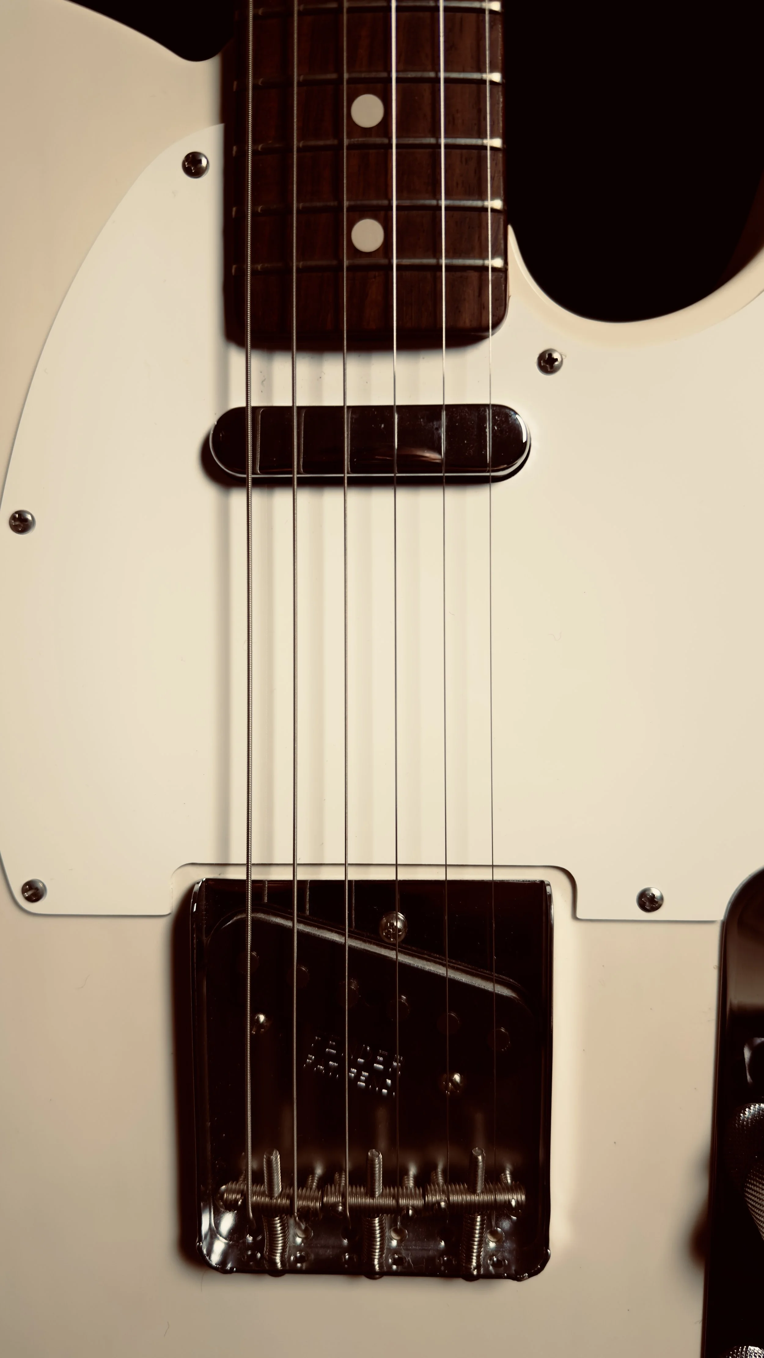 Close-up of a white electric guitar focusing on the strings, pickups, and part of the fretboard.