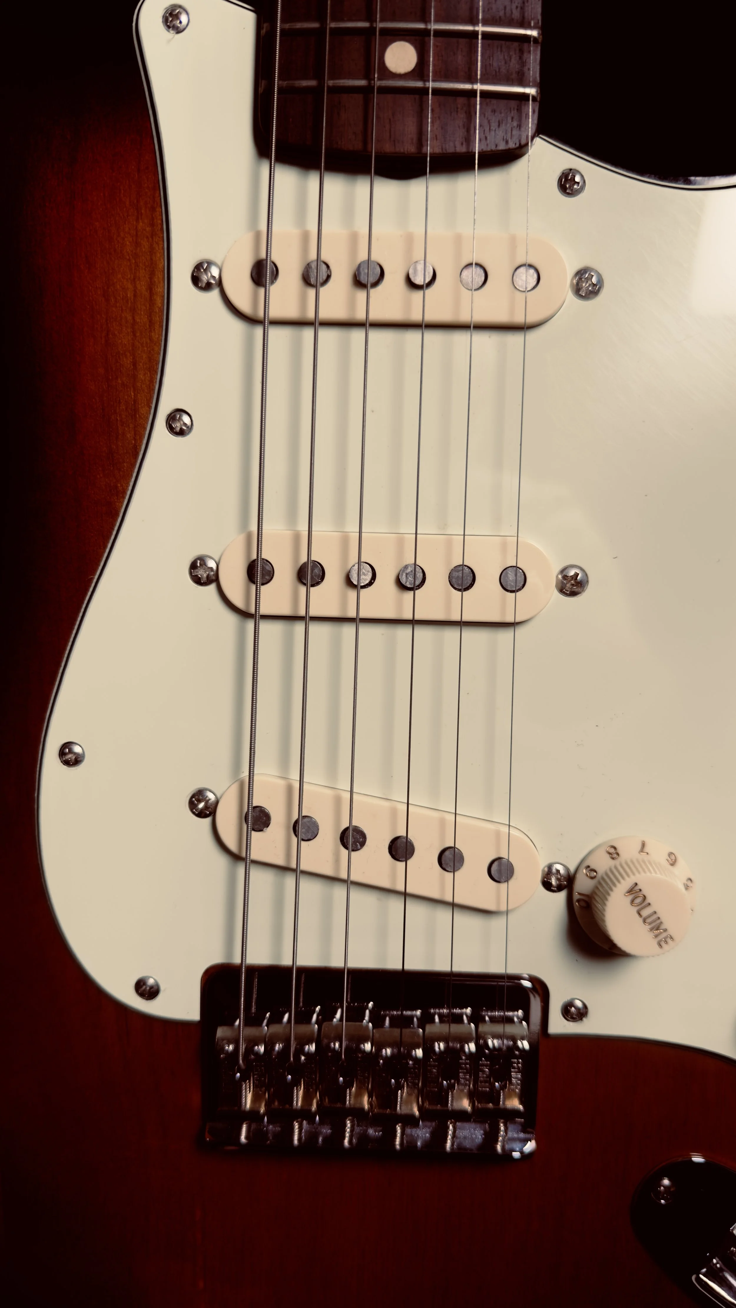 Close-up of an electric guitar showing three pickups, volume knob, strings, and part of the wooden body.