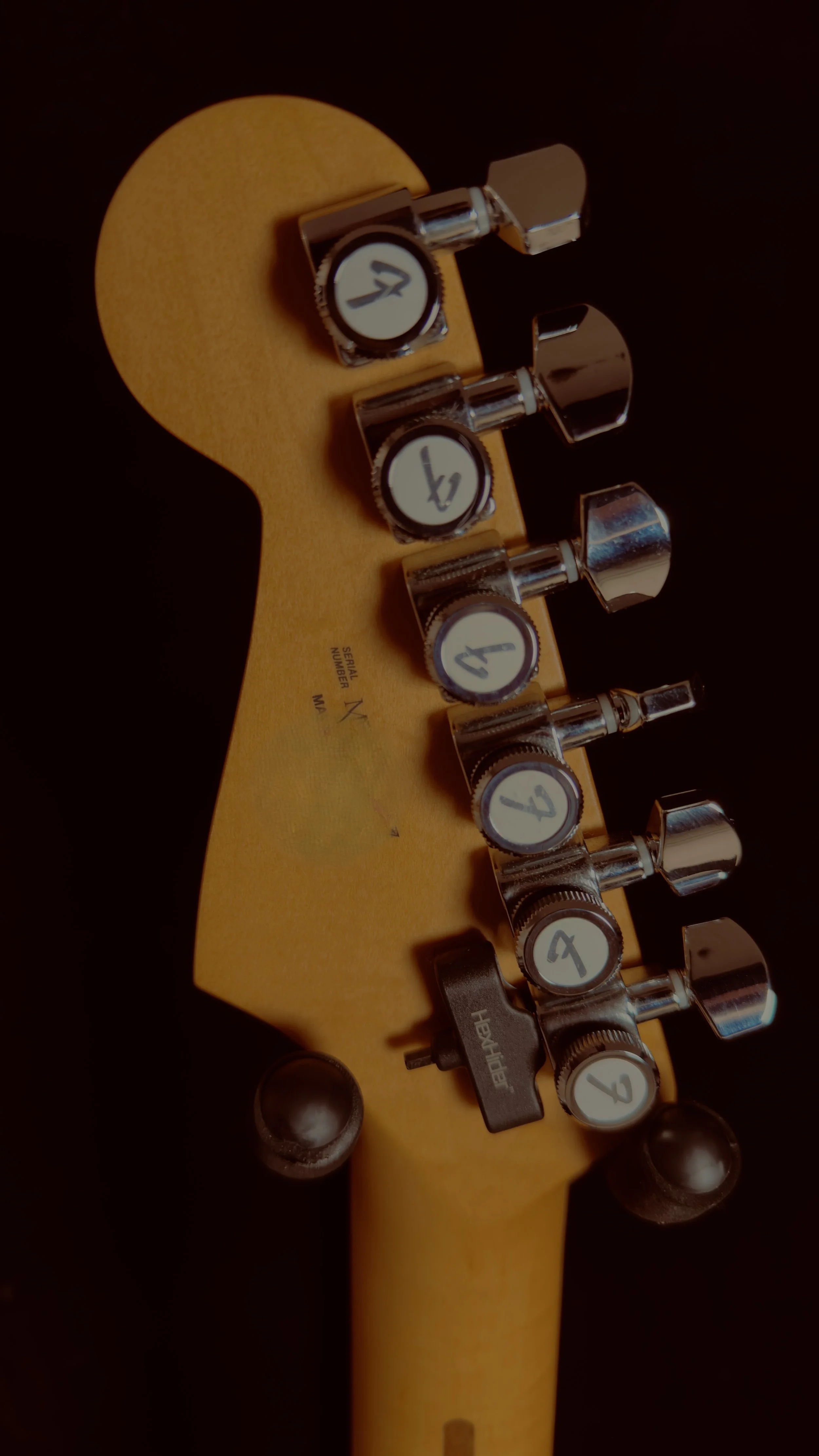 Close-up of the tuning pegs and headstock of a yellow electric guitar, showing six chrome tuning pegs and numbered rotary tuners.