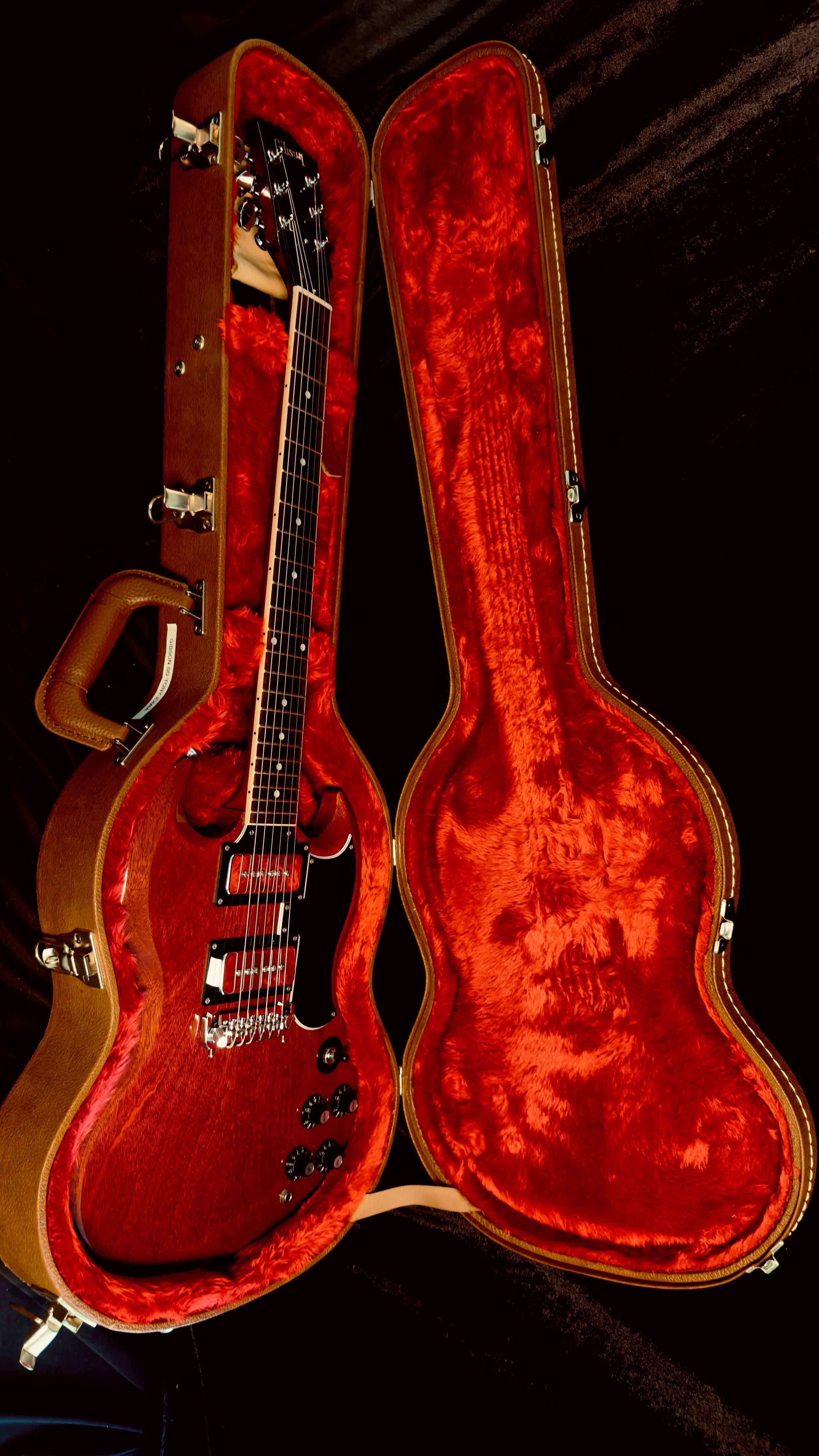 A red electric guitar inside a vintage-style hard case with red plush lining, open on a dark surface.