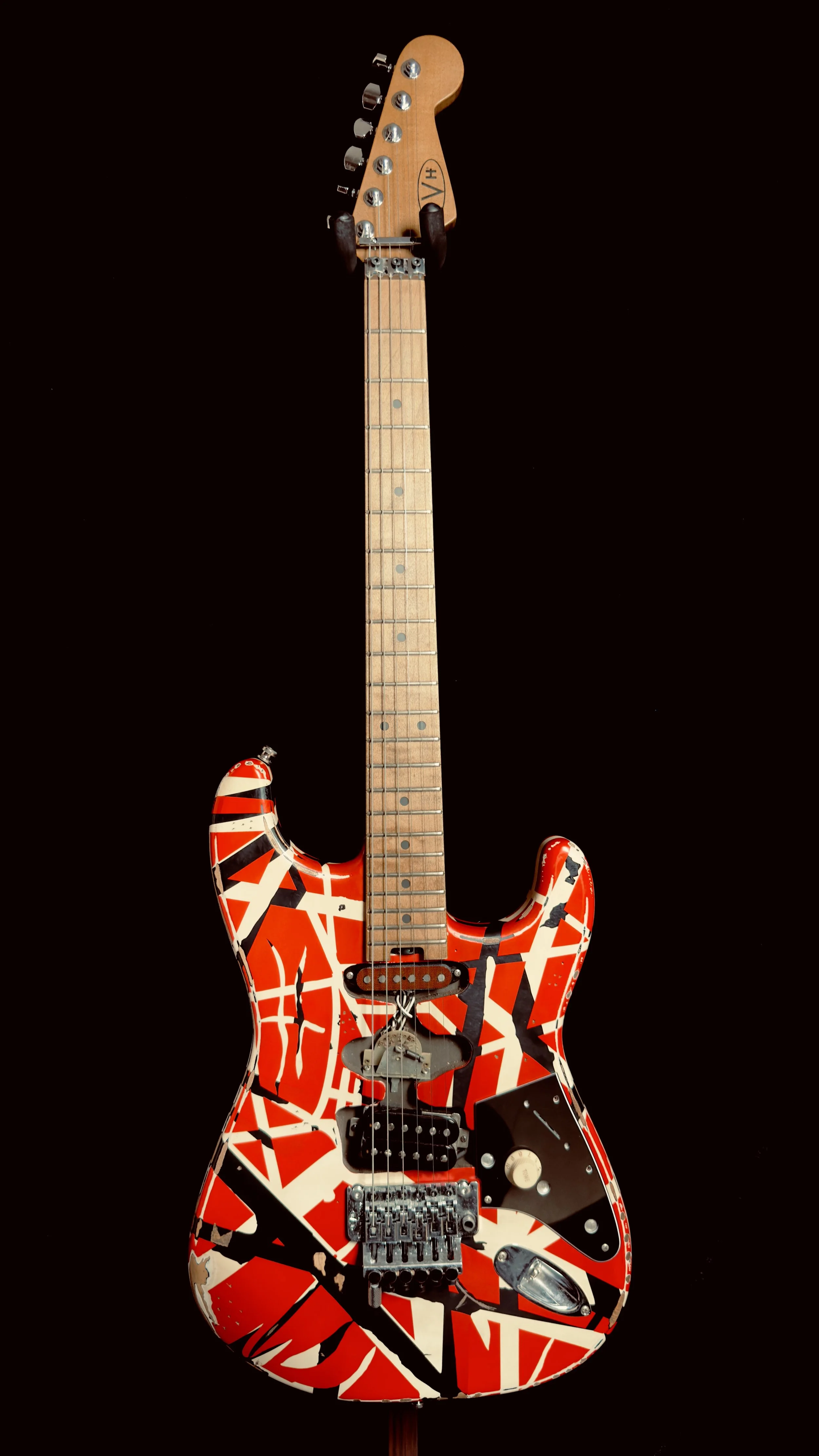 Electric guitar with a red, white, and black abstract paint splatter design on its body, set against a black background.