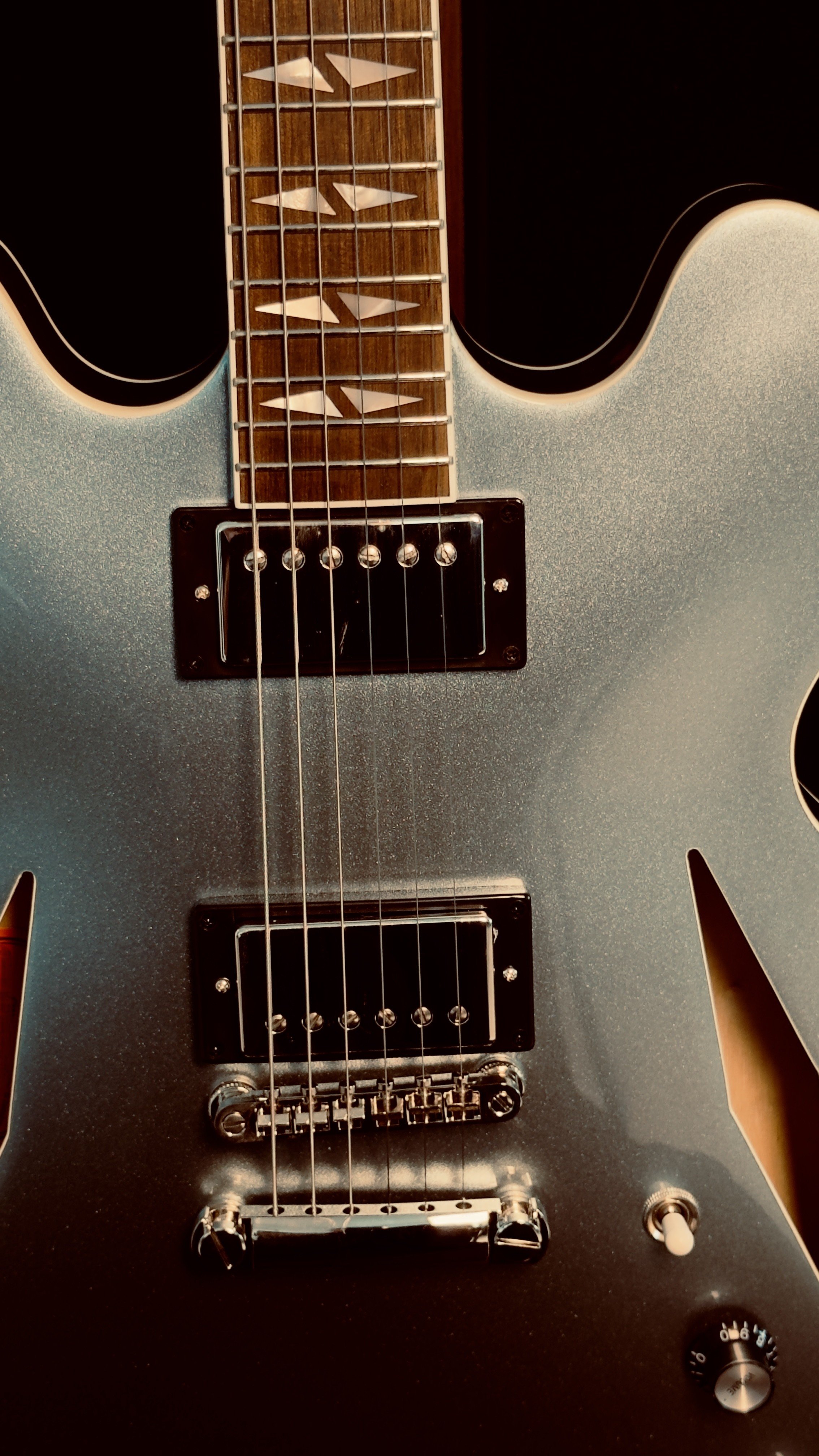 Close-up of an electric guitar with a metallic silver body, black pickups, and a wooden fretboard with diamond inlays.