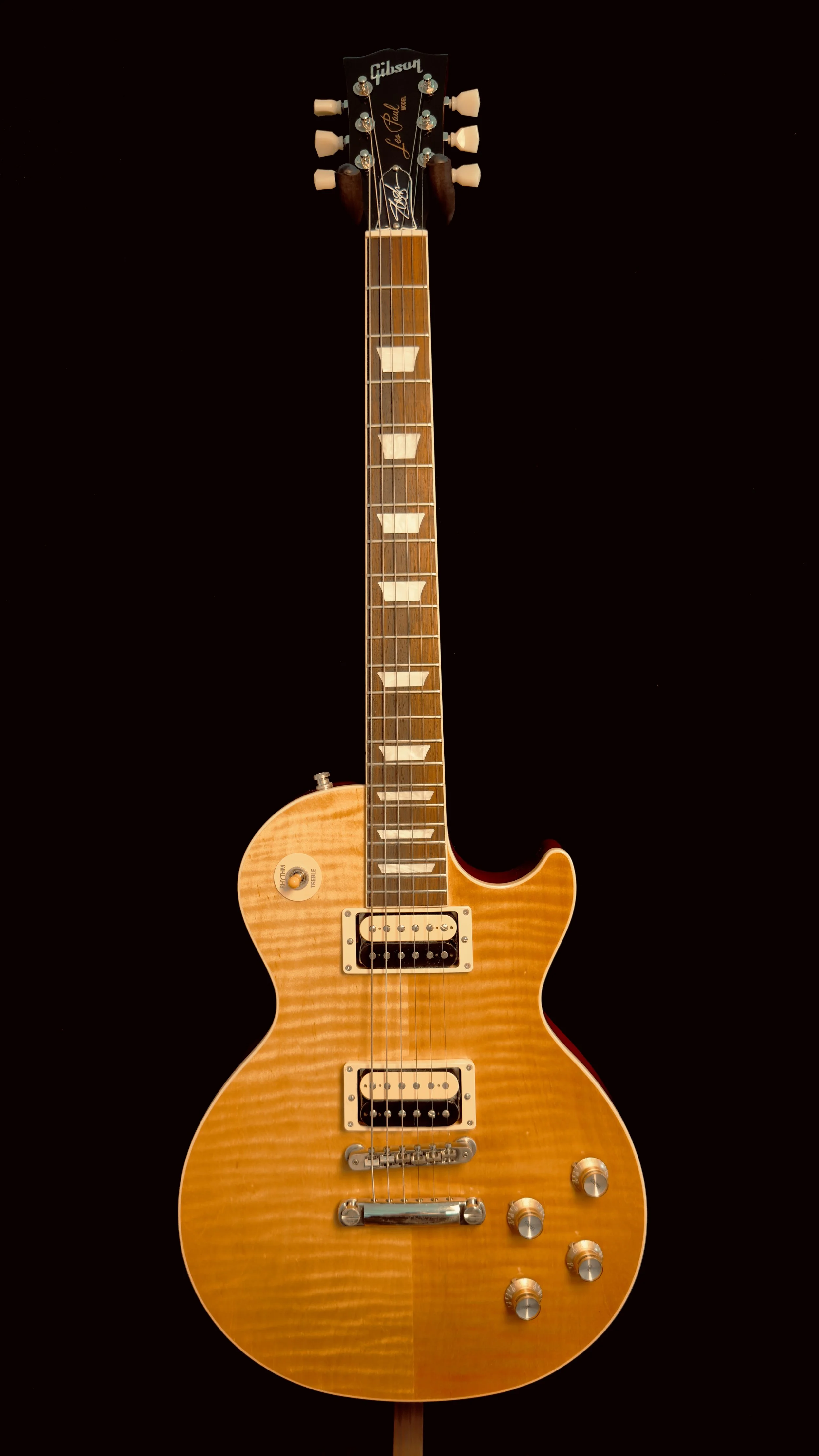 A Gibson electric guitar with a sunburst finish, six tuning pegs, and two humbucker pickups, set against a black background.