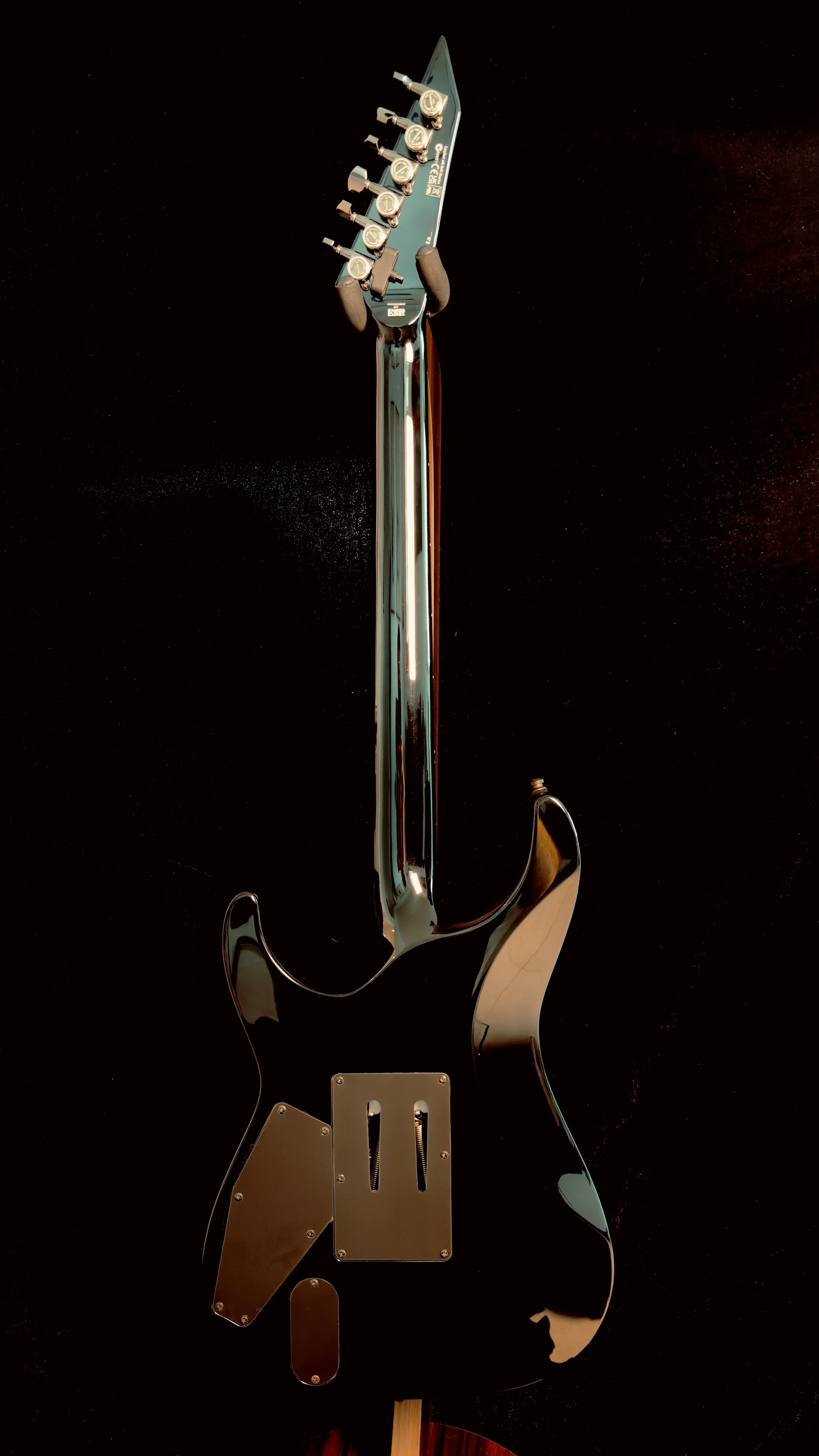 Back of a metallic electric guitar with tuning pegs, bridge, pickup cavity, and strap button visible, resting on a dark surface.