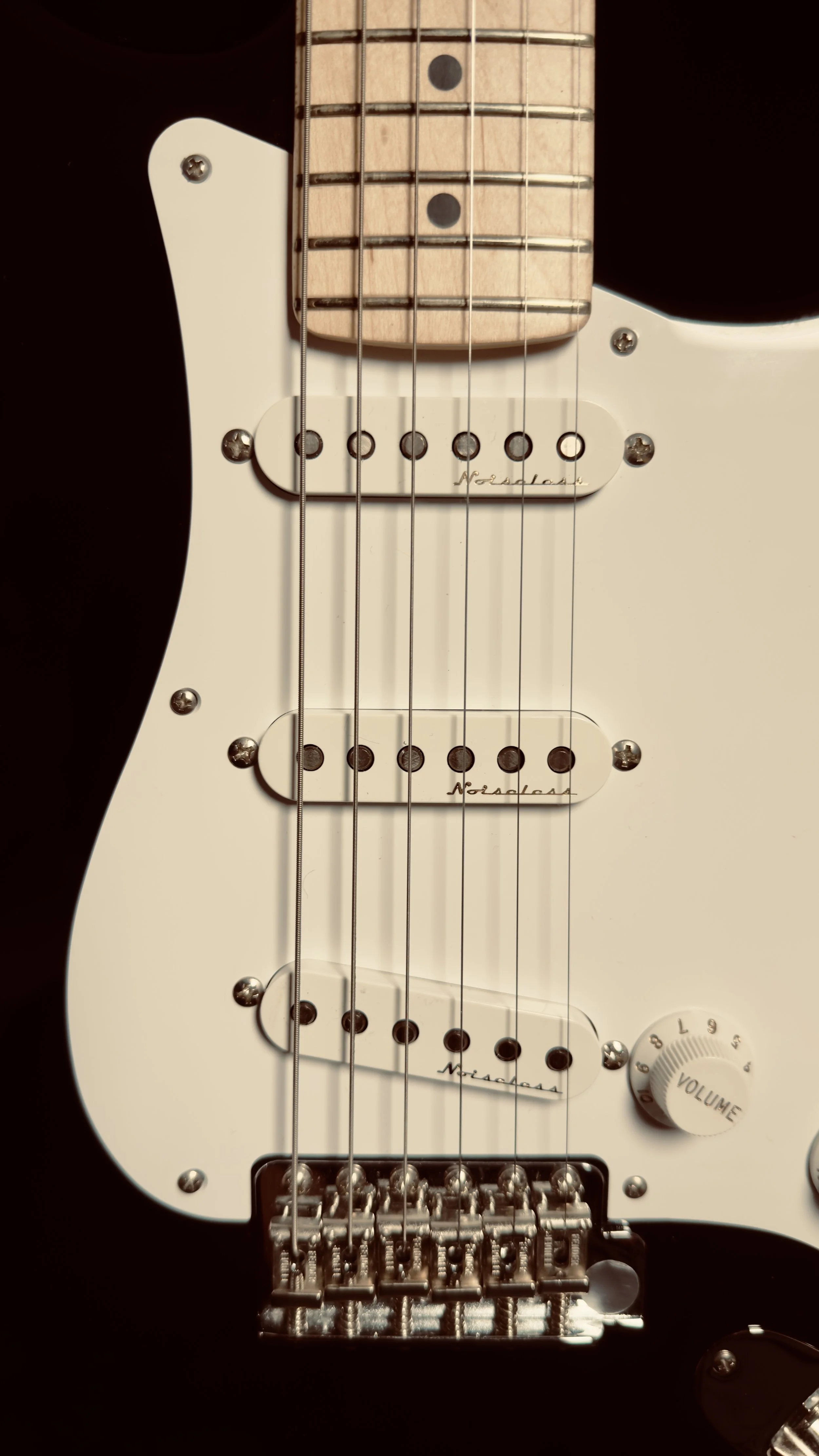 Close-up of an electric guitar with a black body, white pickguard, three single-coil pickups, and a volume knob.