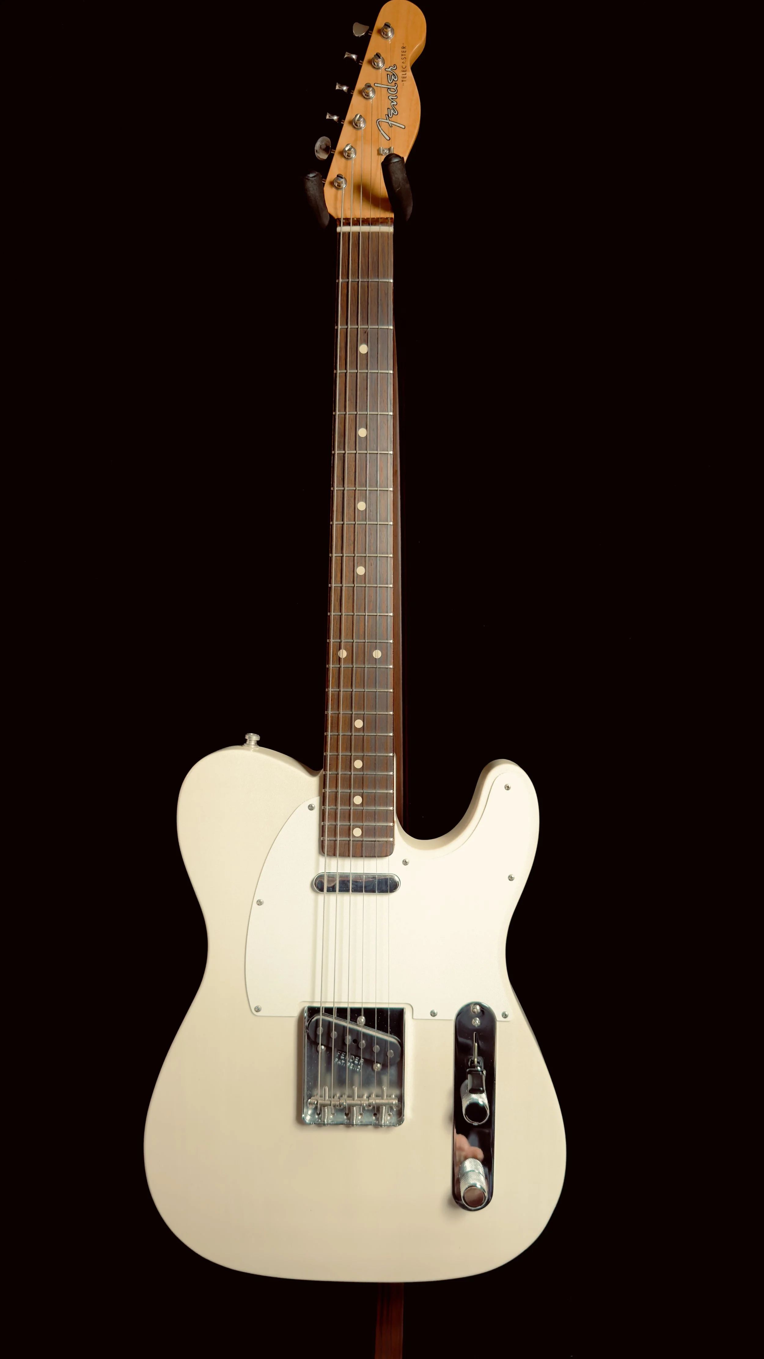 A cream-colored Fender electric guitar with a wooden neck and a white pickguard, set against a black background.