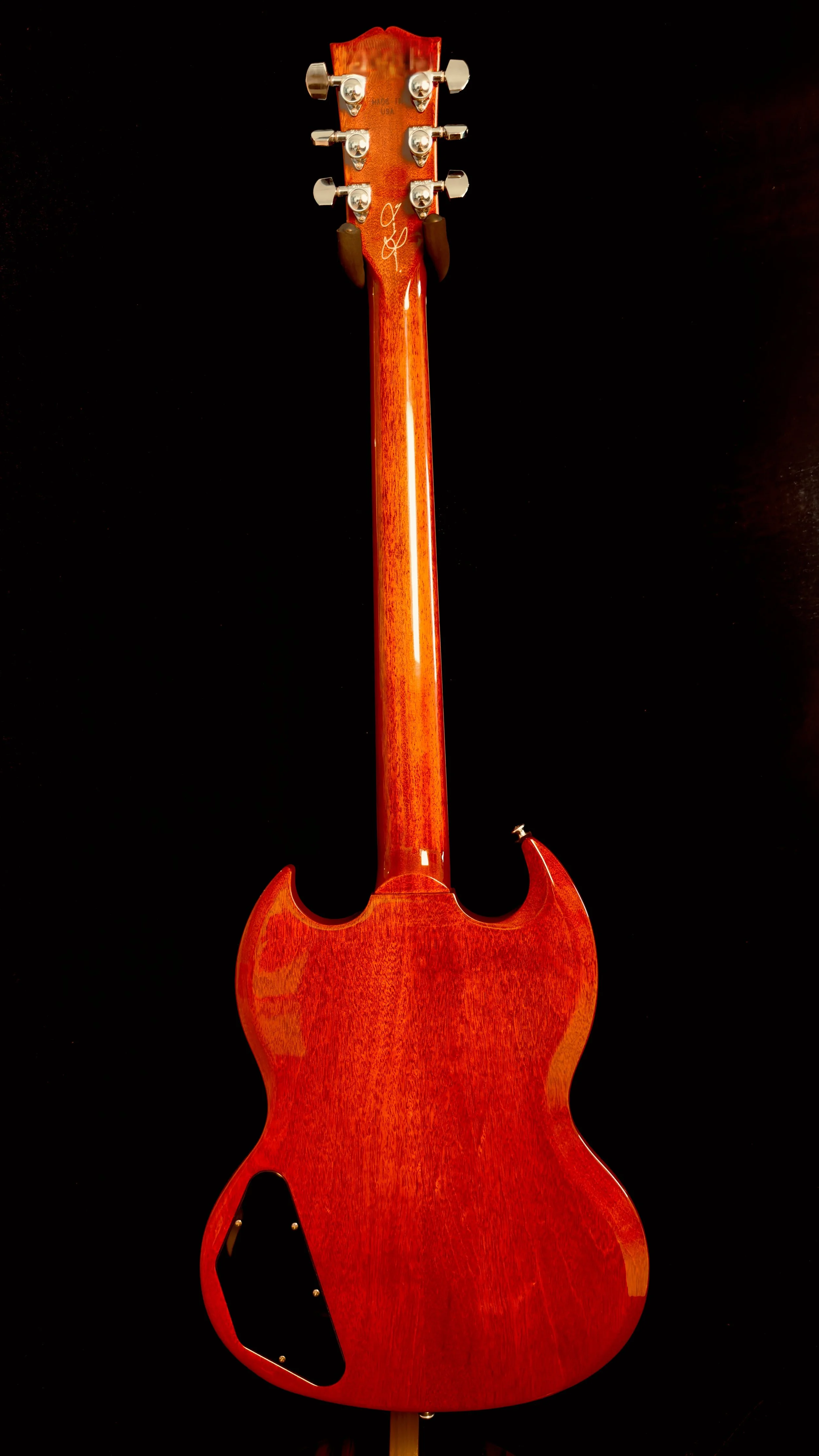 Back of a wooden electric guitar with a red finish, showing the neck and body, on a black background