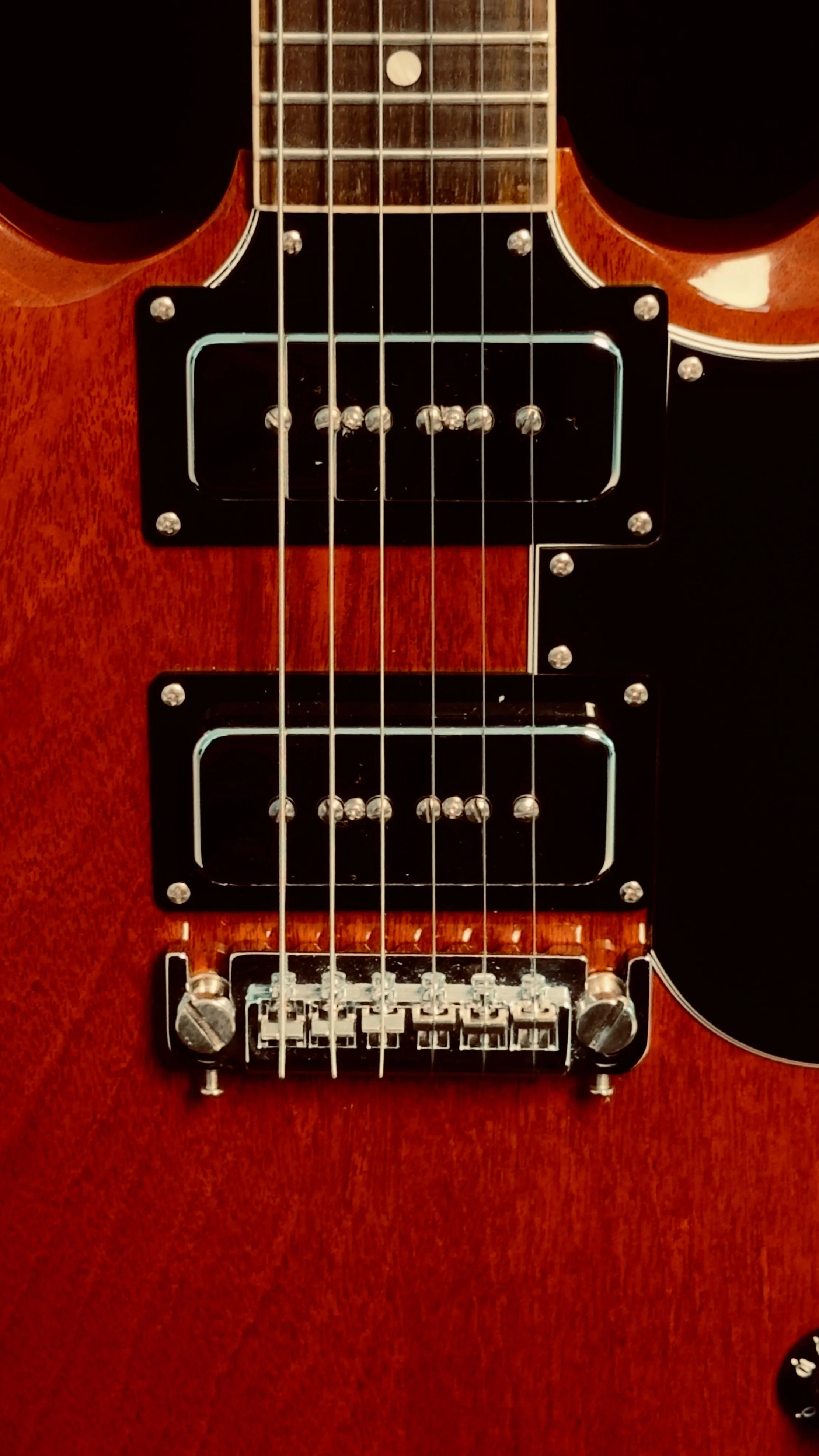 A close-up of a red electric guitar with black pickups and a chrome bridge.