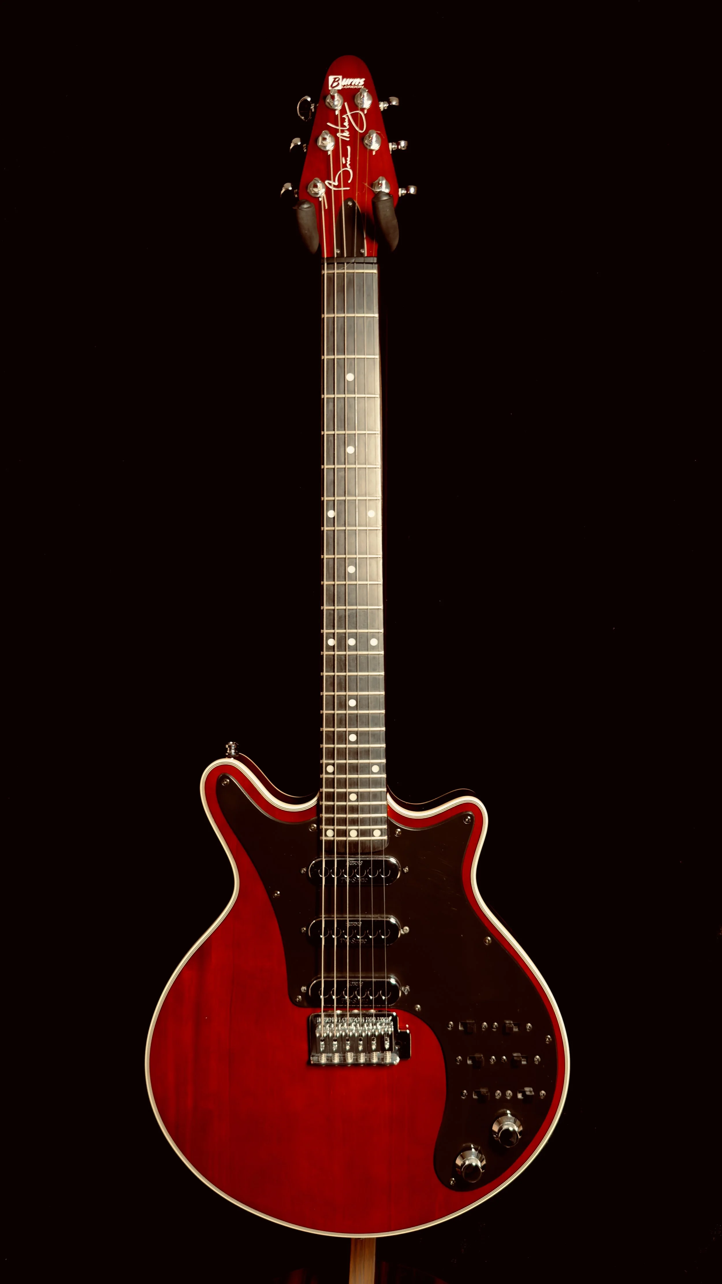 Red electric guitar with a black pickguard and multiple control knobs, set against a black background.