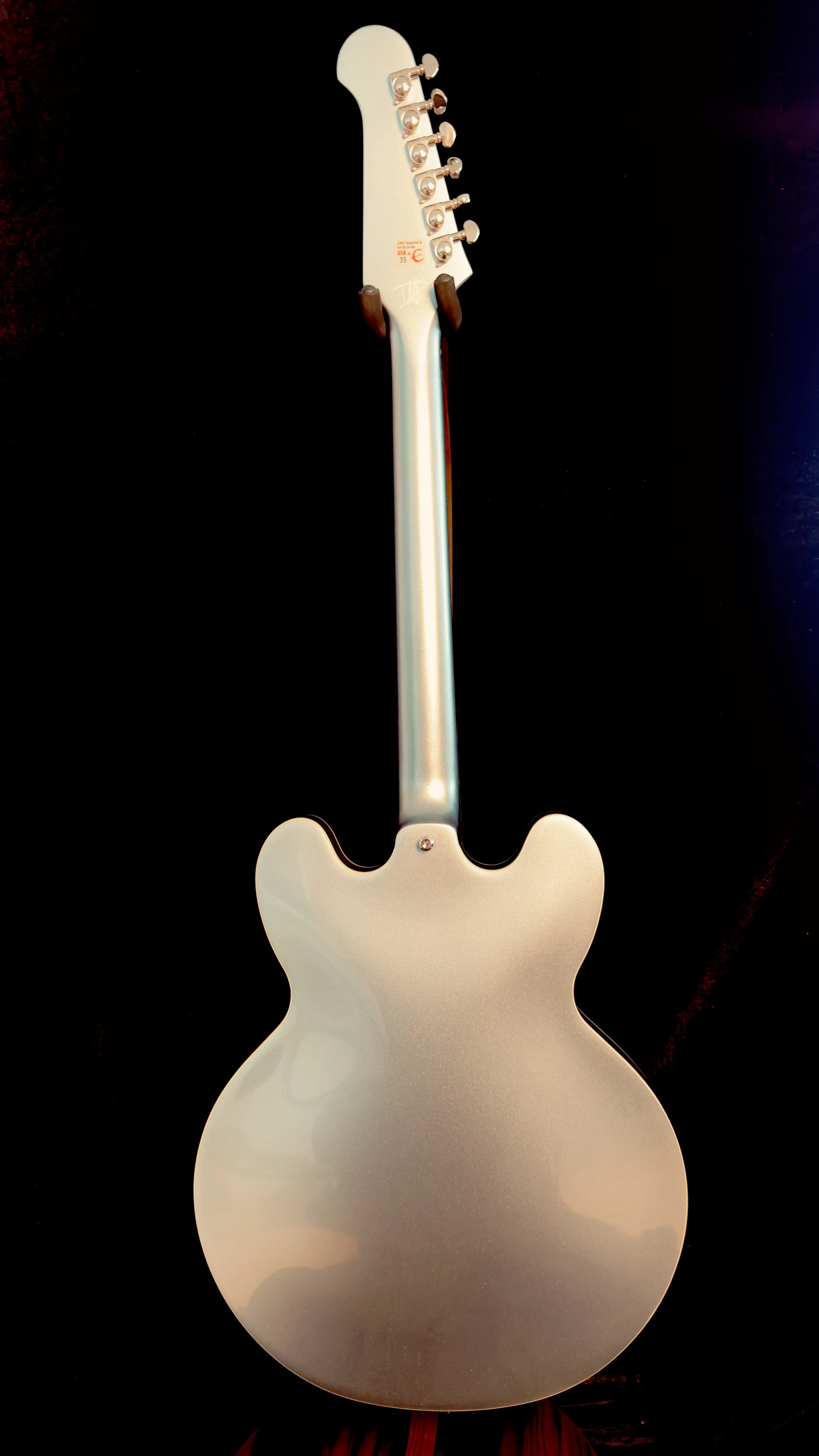Back of an electric guitar with a metallic finish, showing the headstock, neck, and body on a black background.