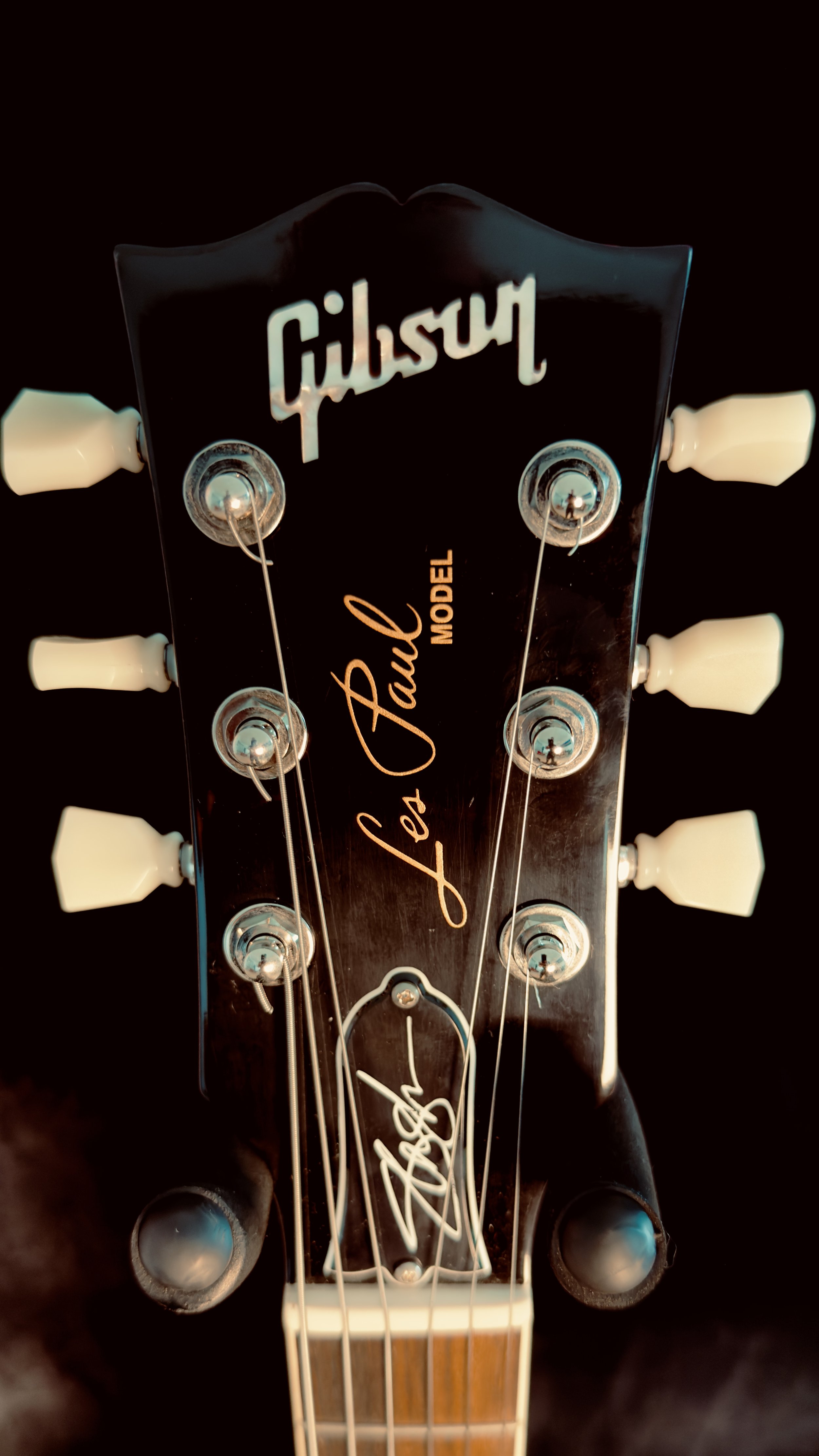 Close-up of the headstock of a black Gibson Les Paul Standard electric guitar with white tuning pegs and a signature on the headstock.