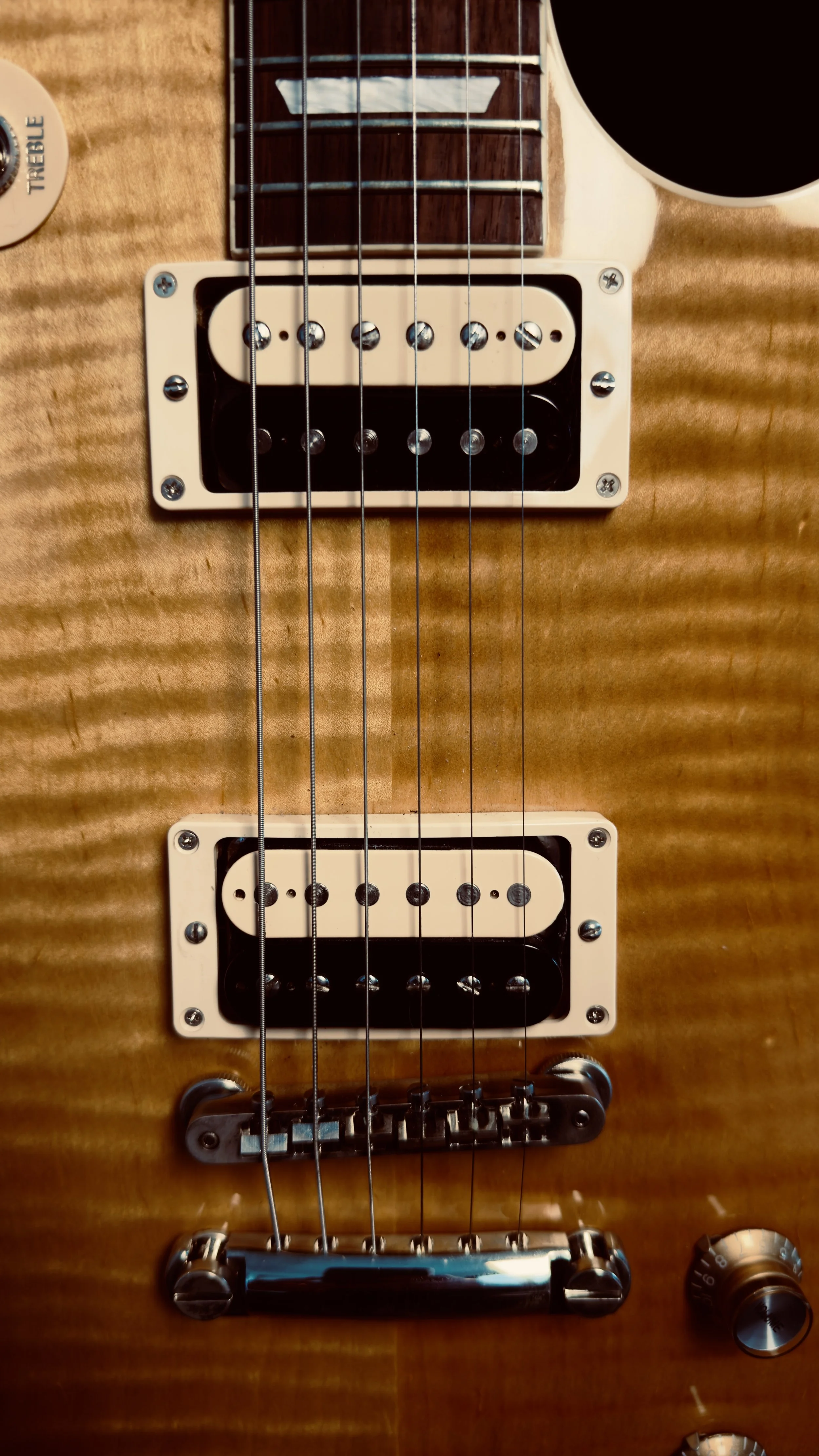 Close-up of a wooden electric guitar with two humbucker pickups, a bridge, and control knobs.