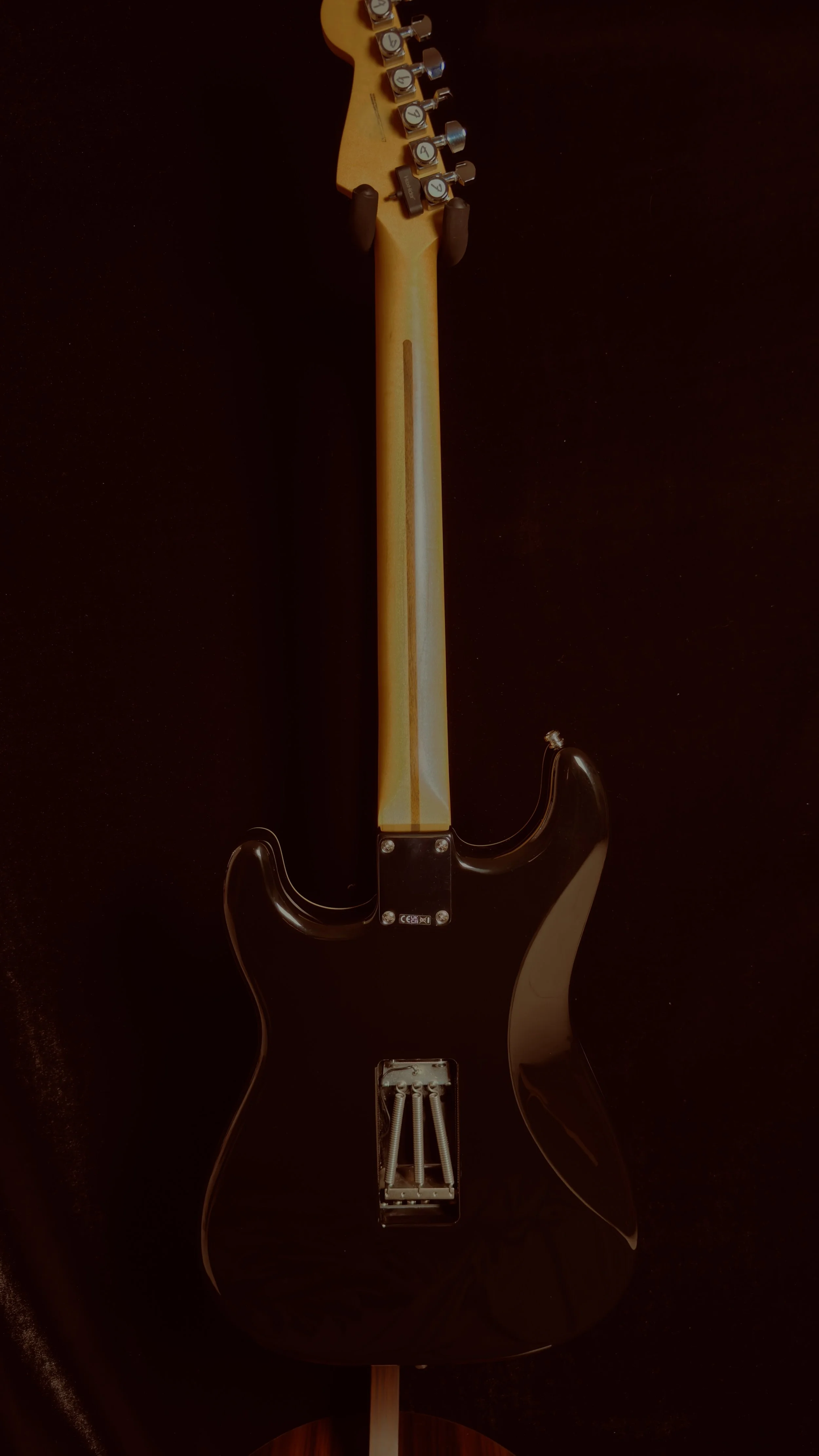 Back of an electric guitar with a black body and a natural wood neck, shown against a black background.