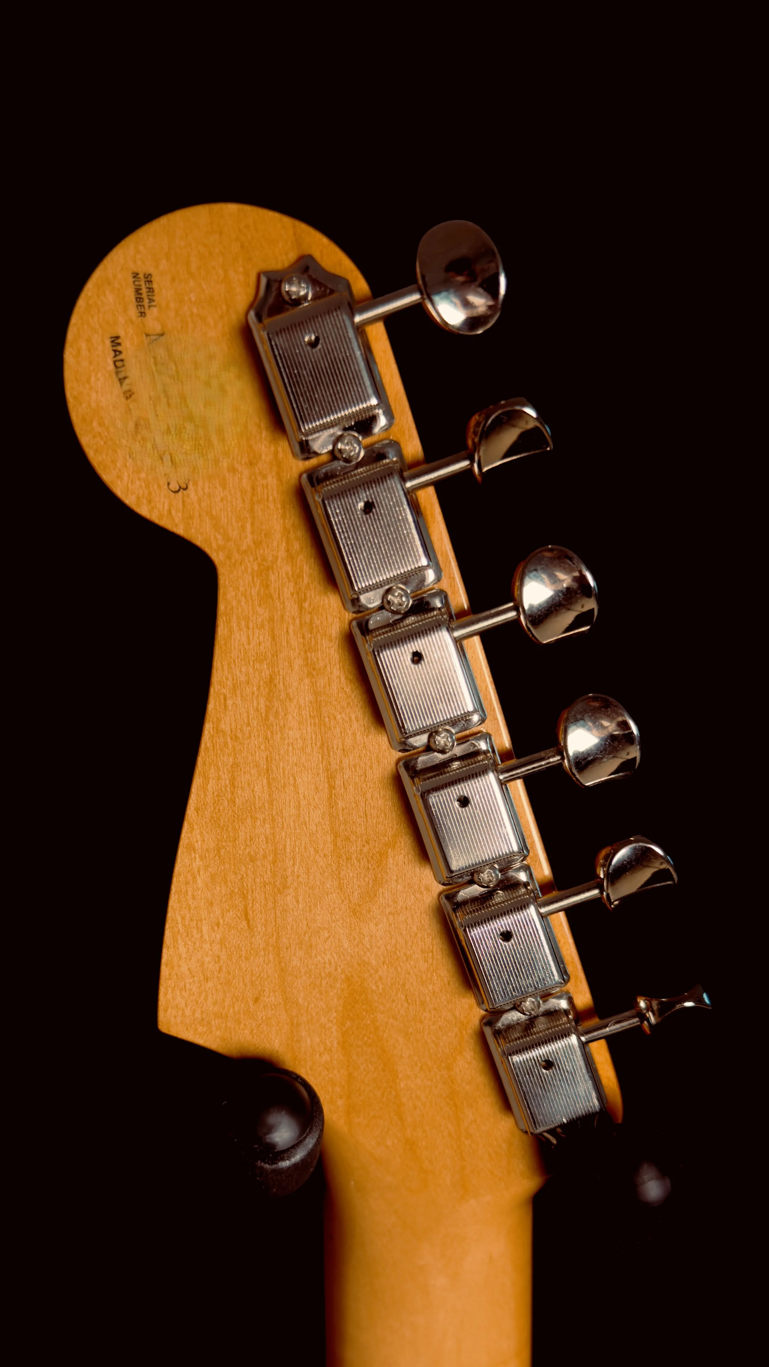 Close-up of the tuning pegs and headstock of an electric guitar with a natural wood finish and black background.