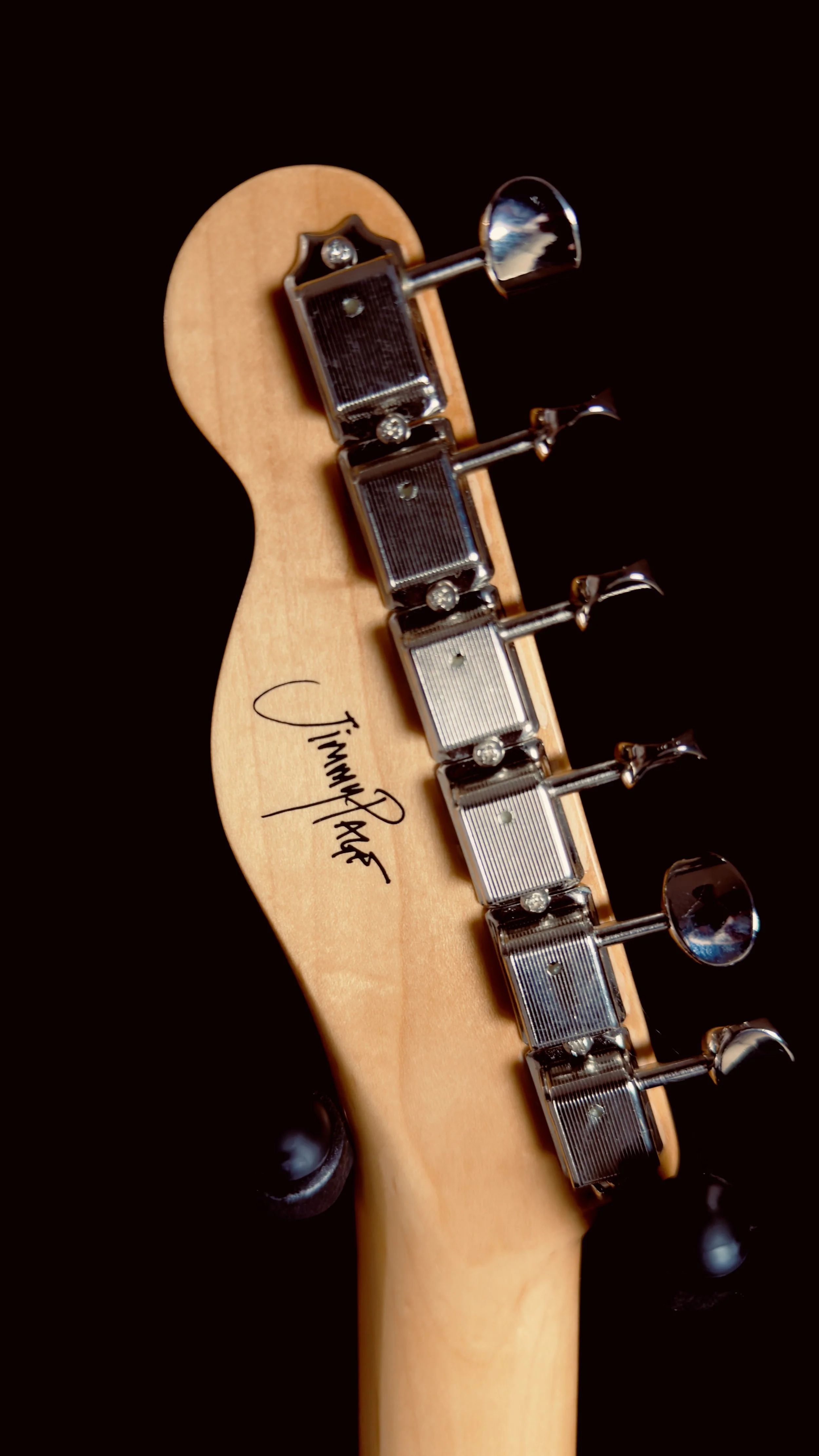 Close-up of the headstock of a guitar with four tuning pegs, featuring a signature that reads "Jimmy Page."