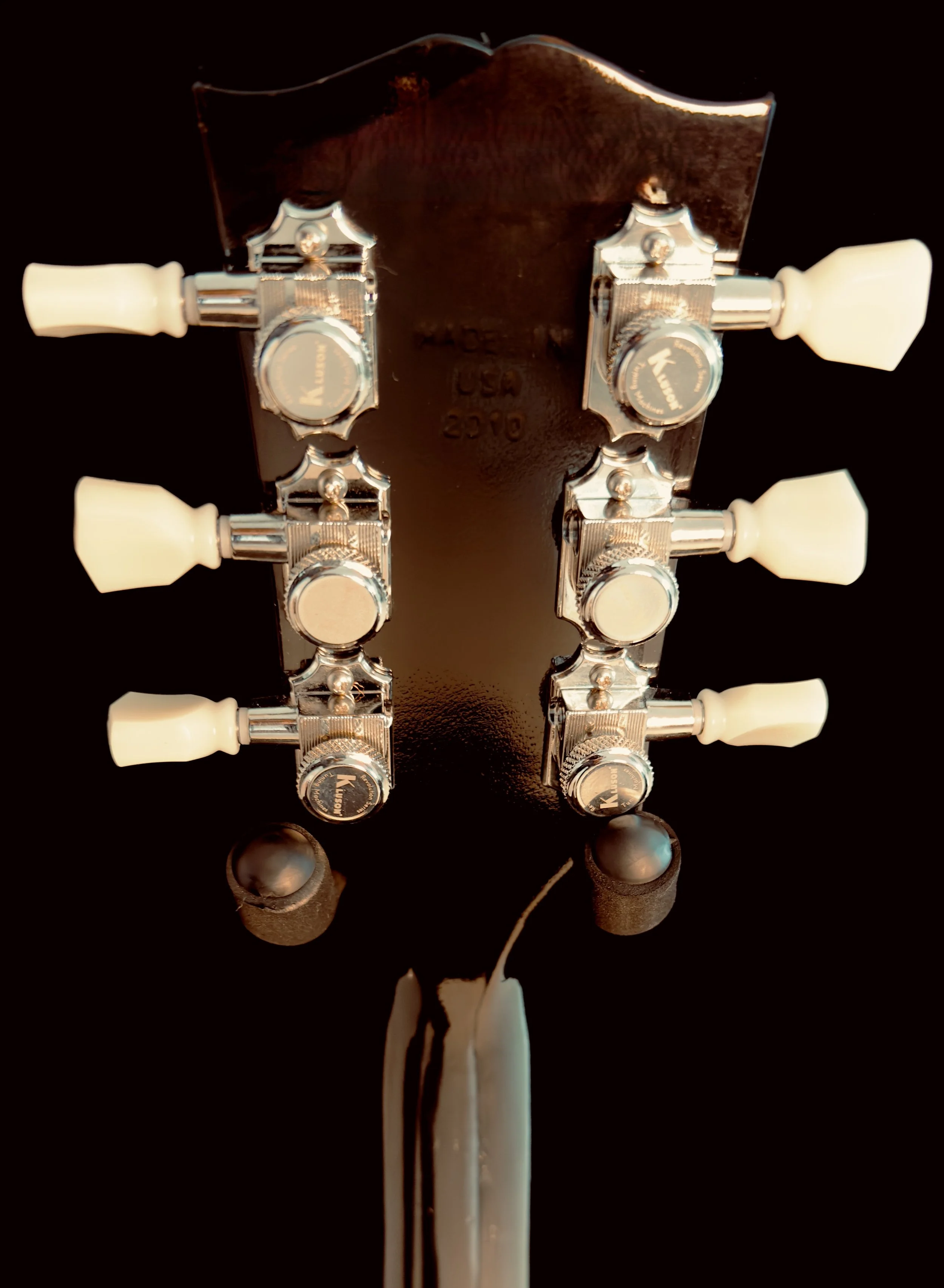 Close-up of the back of a guitar headstock showing six tuning pegs with white tuning keys, metal hardware, and a black background.