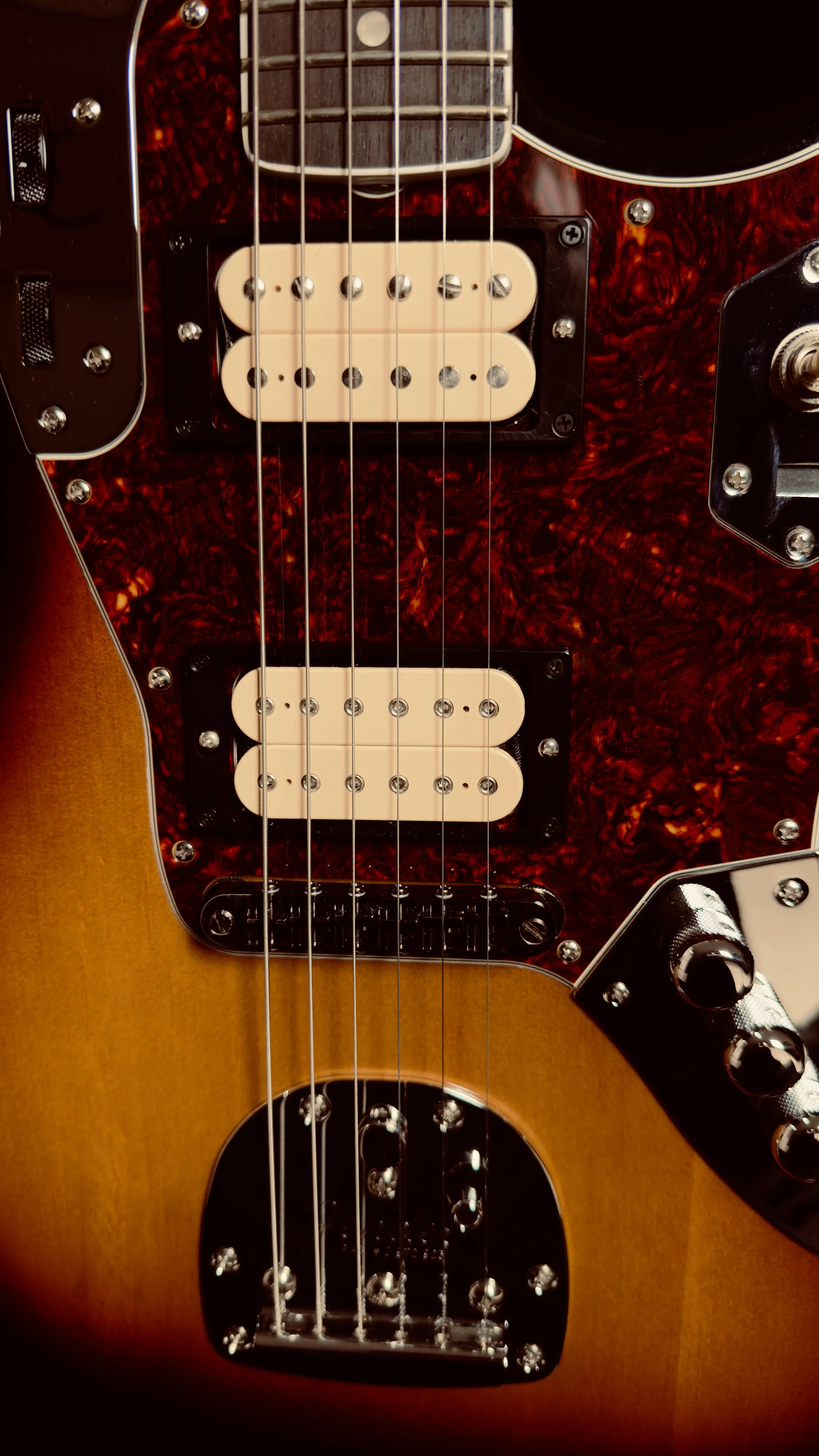 Close-up of a vintage electric bass guitar with a sunburst finish, featuring dual humbucker pickups, control knobs, and a tortoiseshell pickguard.